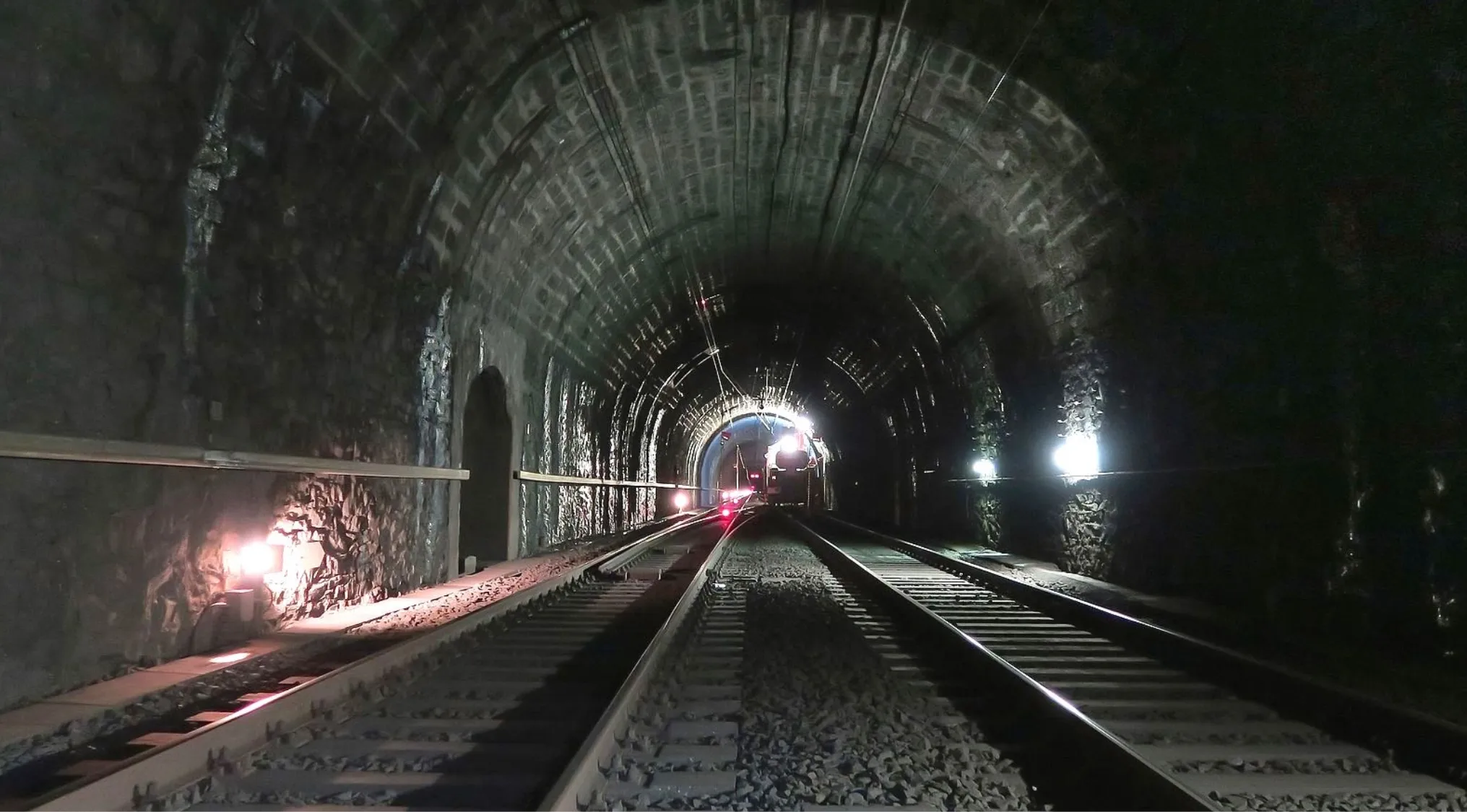 A long, brightly lit pedestrian tunnel with an arched ceiling and people walking, referencing the St. Gotthard tunnel.