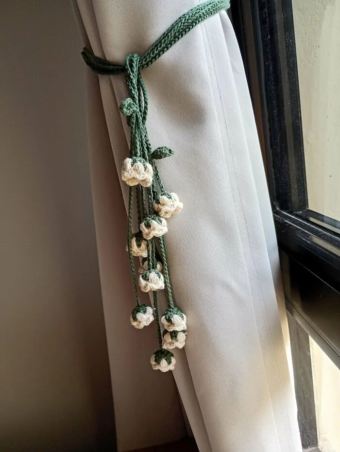 Crocheted curtain tieback with white flowers and green stems on beige curtain