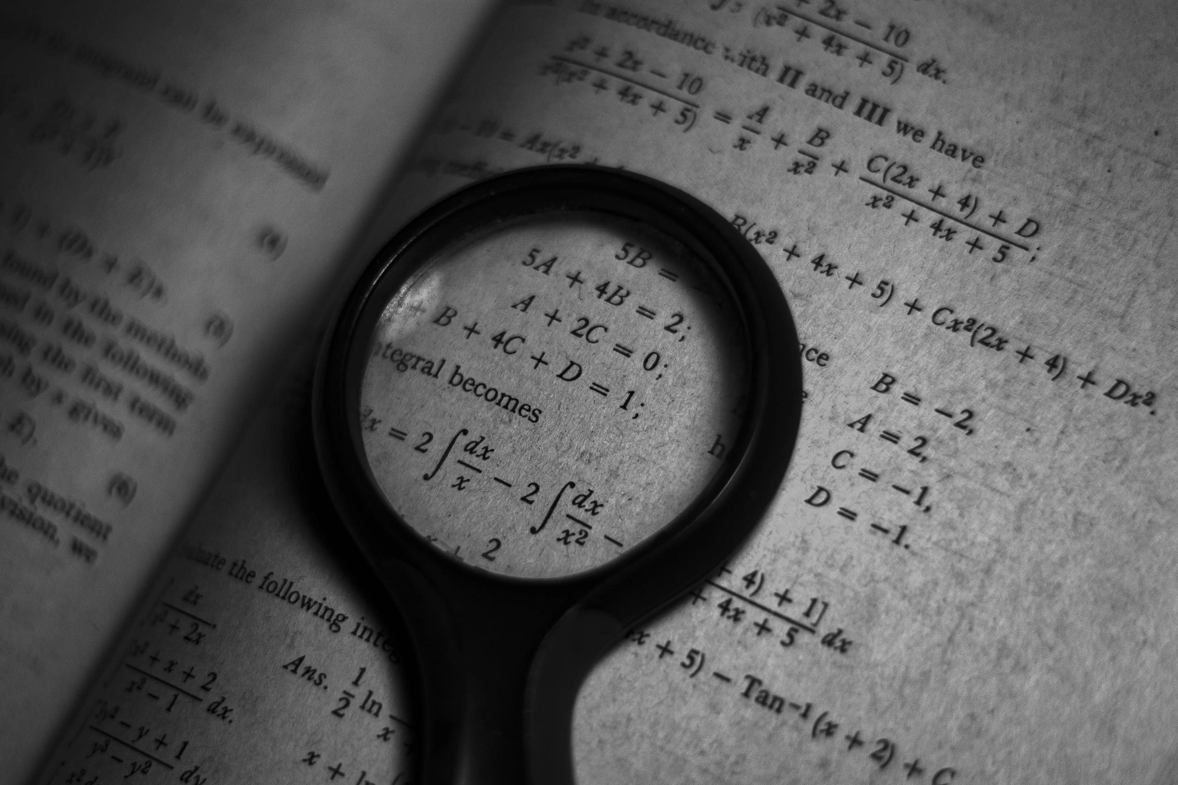 Magnifying glass focusing on algebra equations and formulas printed on an open textbook page in black and white.