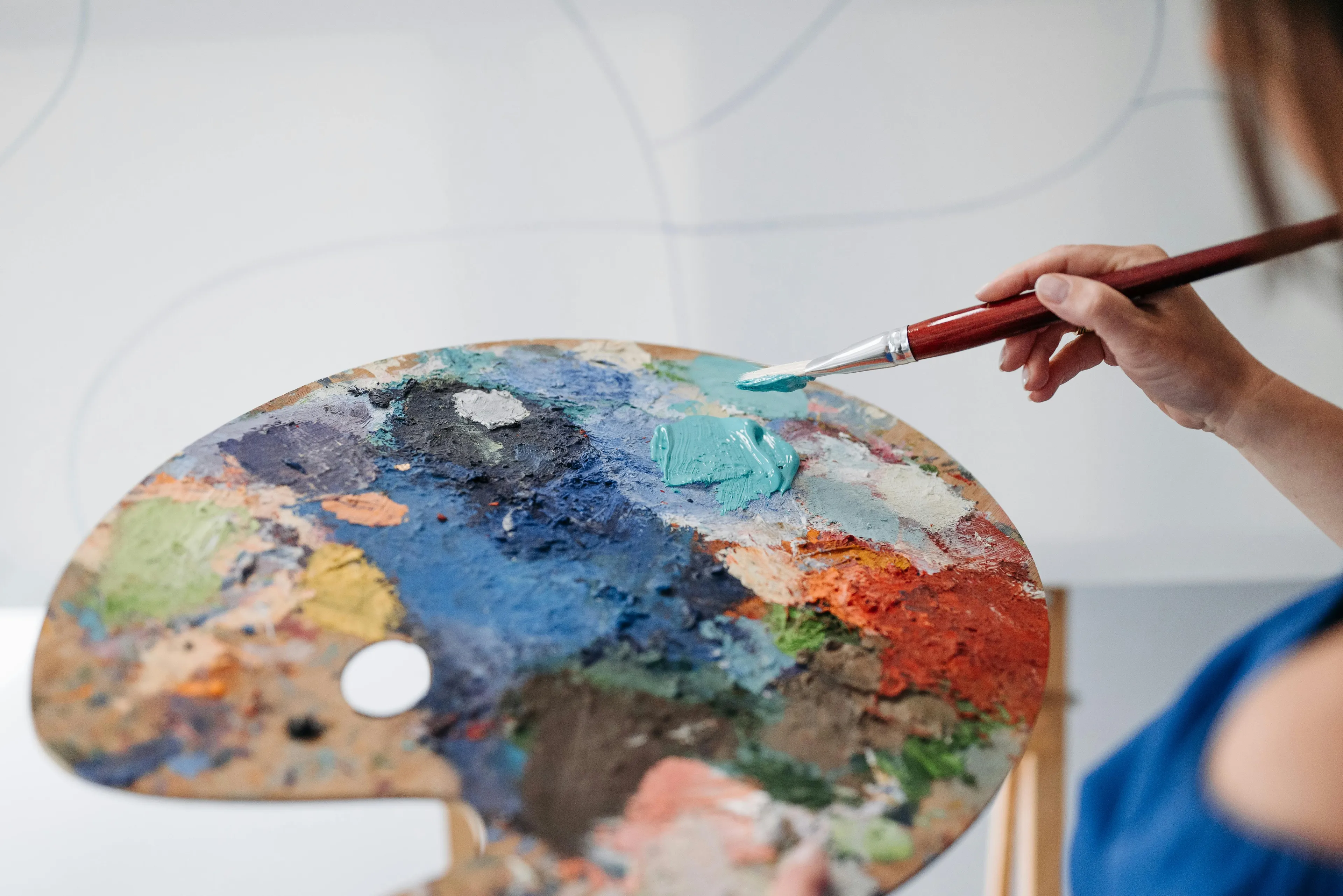 Artist holding a paintbrush and mixing colors on a palette, focusing on the art creation process.