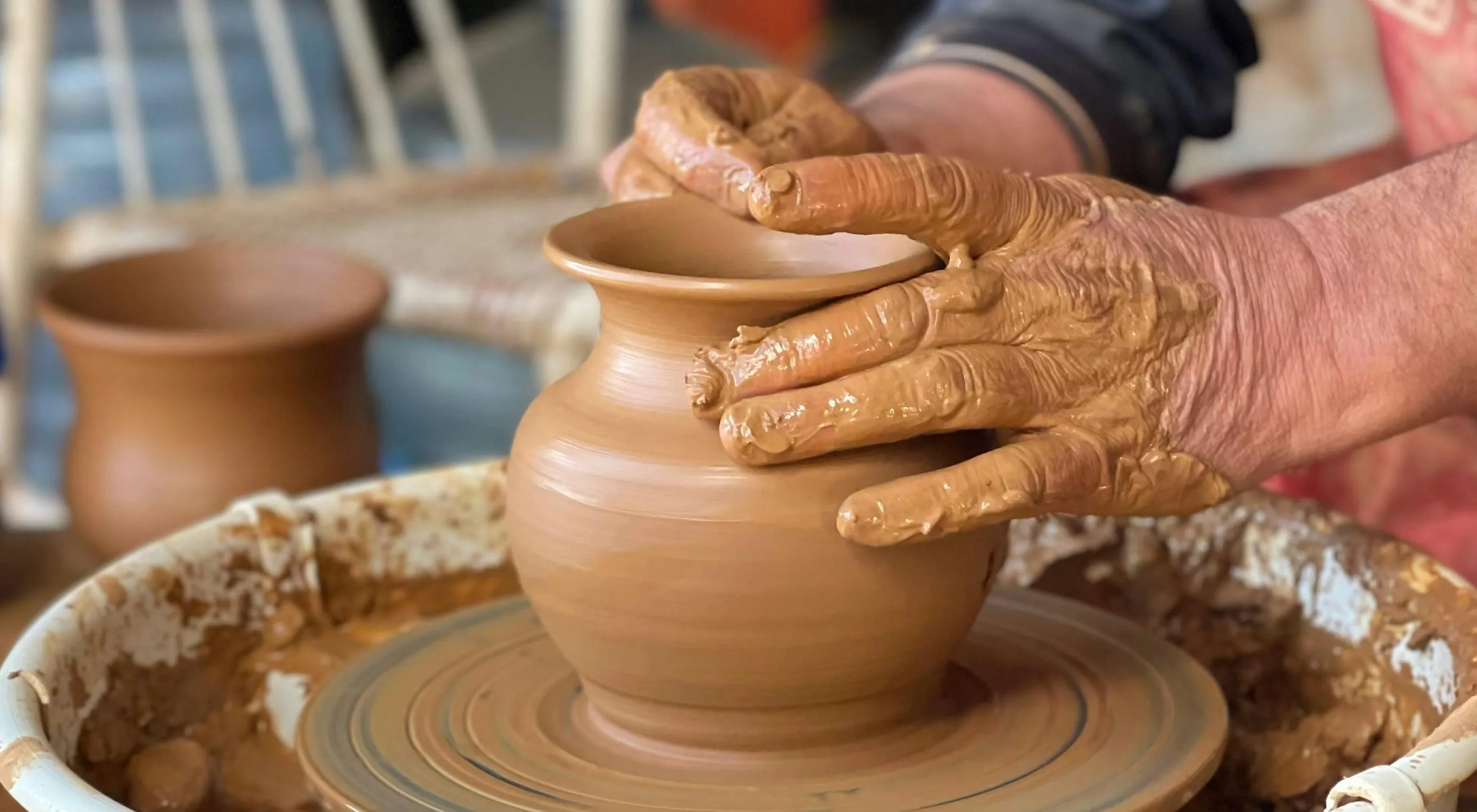 Hands shaping a clay pot on a pottery wheel, demonstrating the process of creating pottery as a relaxing hobby.