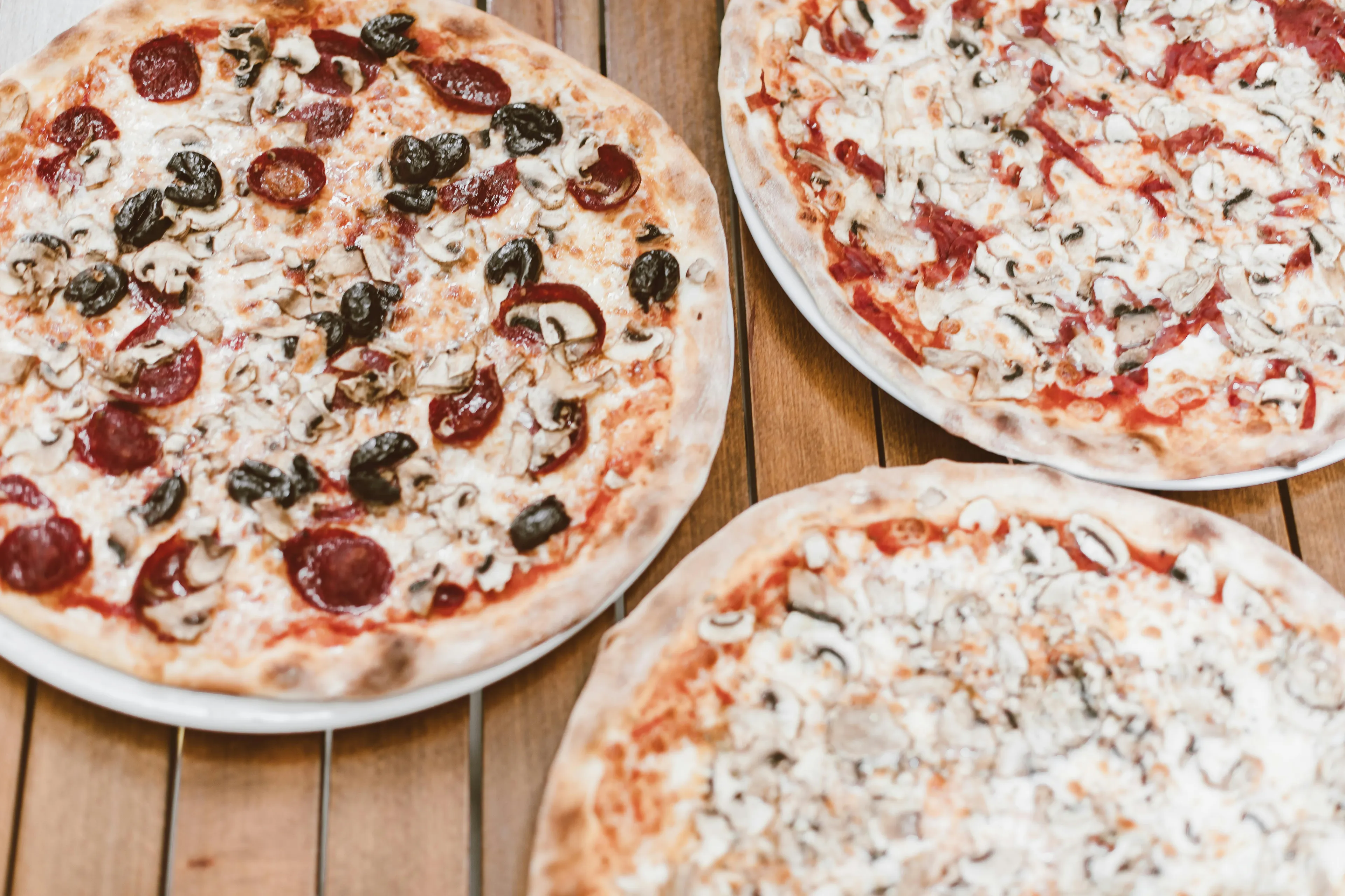 Three different pizzas on plates on a wooden table, illustrating the question are you a left-brain or right-brain pizza choice