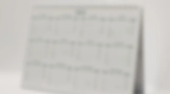 Blurry image of a common desk calendar with unreadable dates and notes on a white surface.