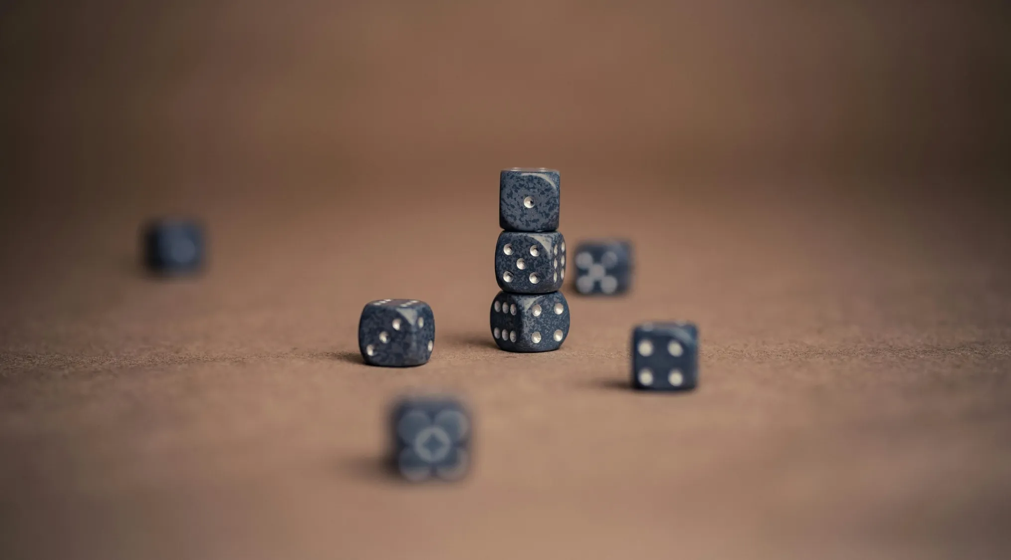 Stacked and scattered six-sided dice on a brown surface illustrating math probability of rolling a number divisible by 3