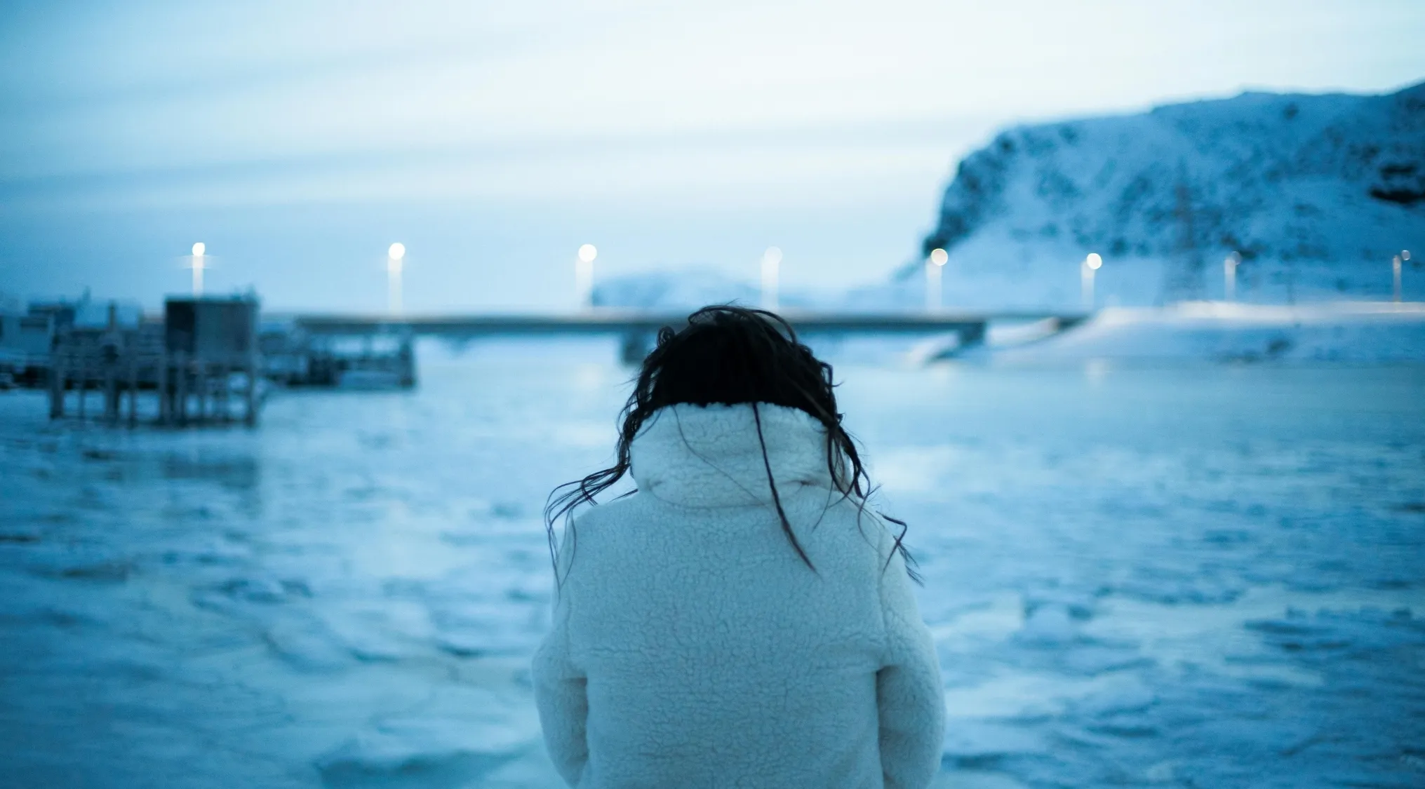 Person wearing white coat standing near icy water representing involuntary action opposite to sweating in biology.