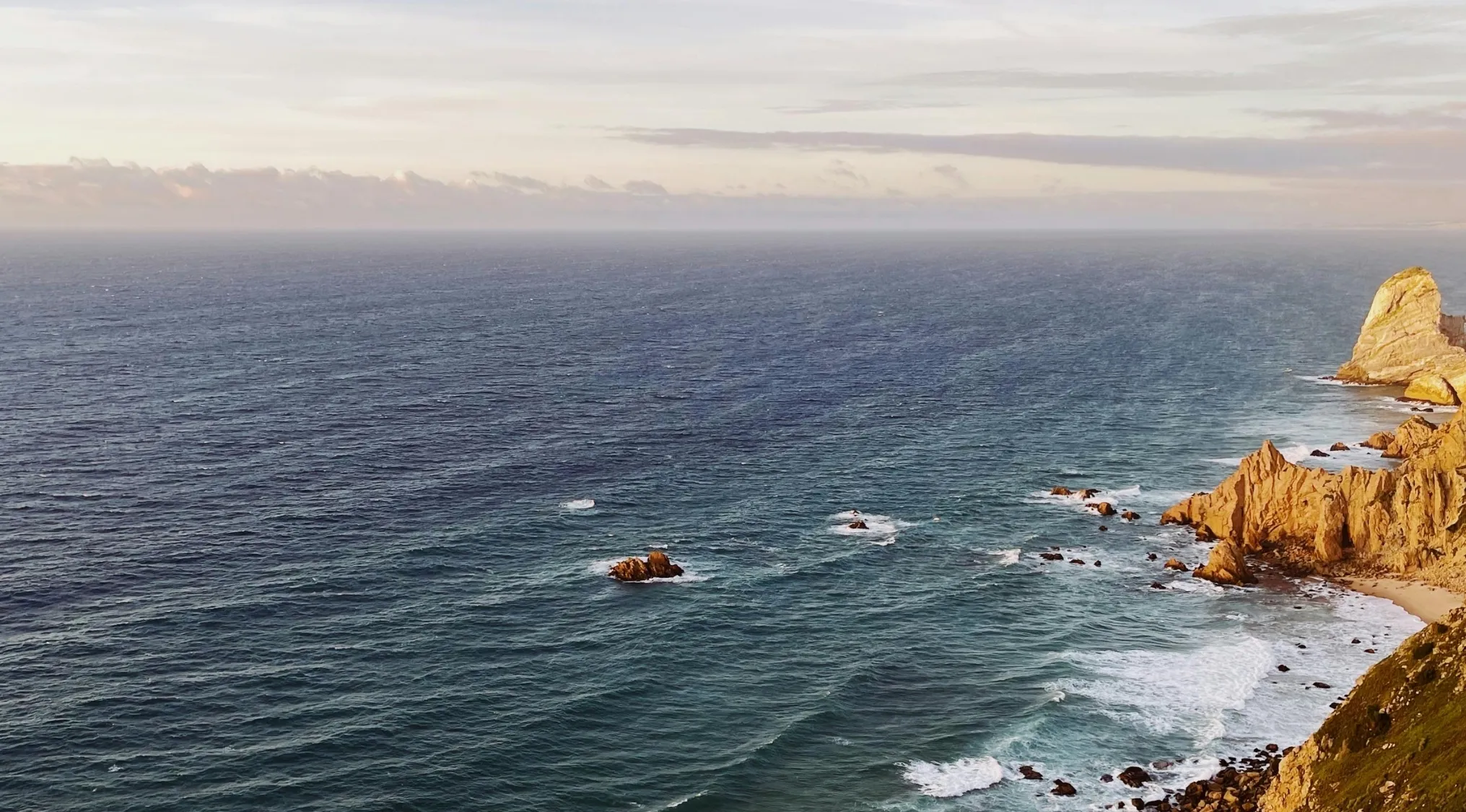 Rocky coastline at sunset with waves crashing and ocean stretching toward horizon for Atlantic Ocean history question.