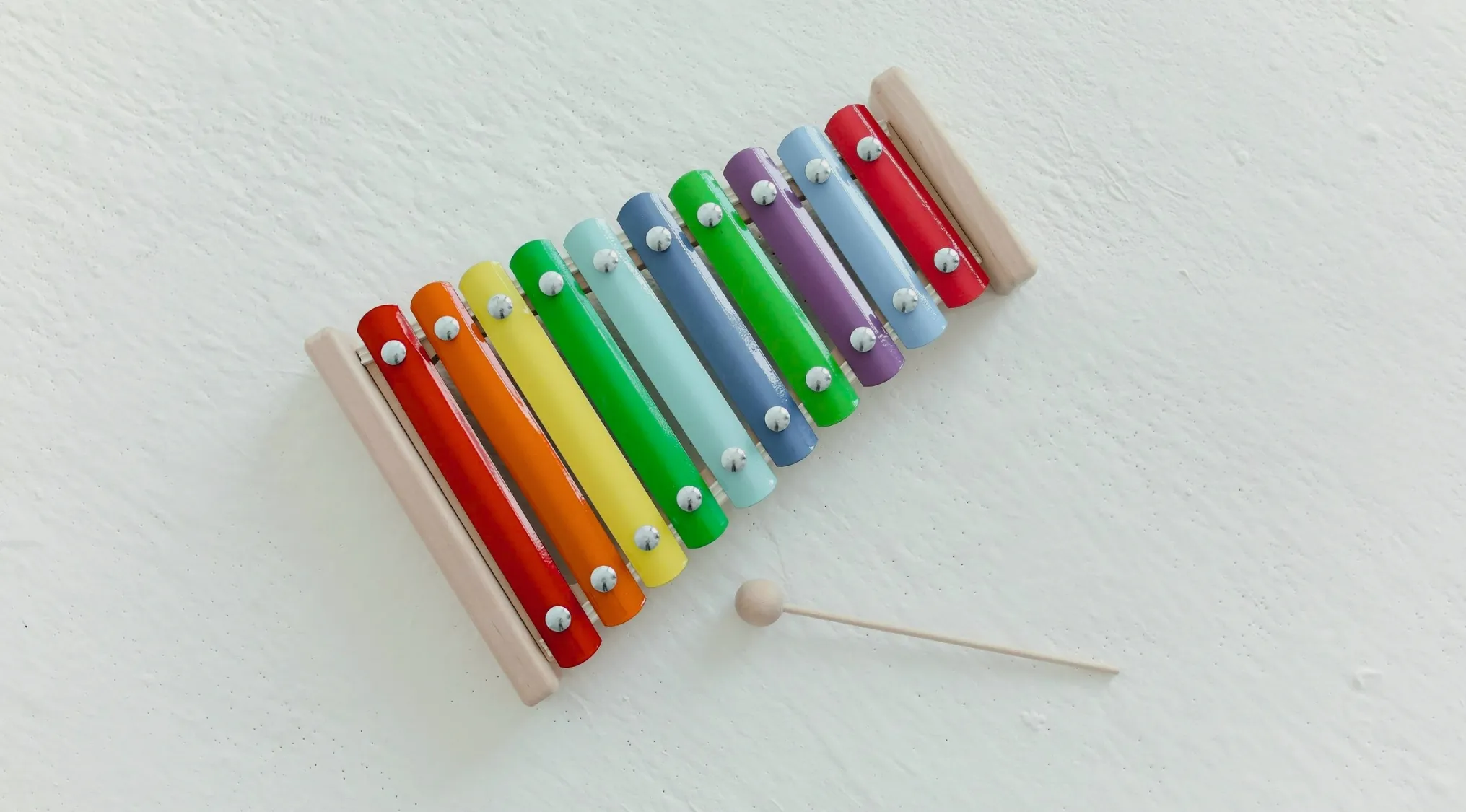 Colorful xylophone musical instrument with wooden mallet on white textured background for school questions music