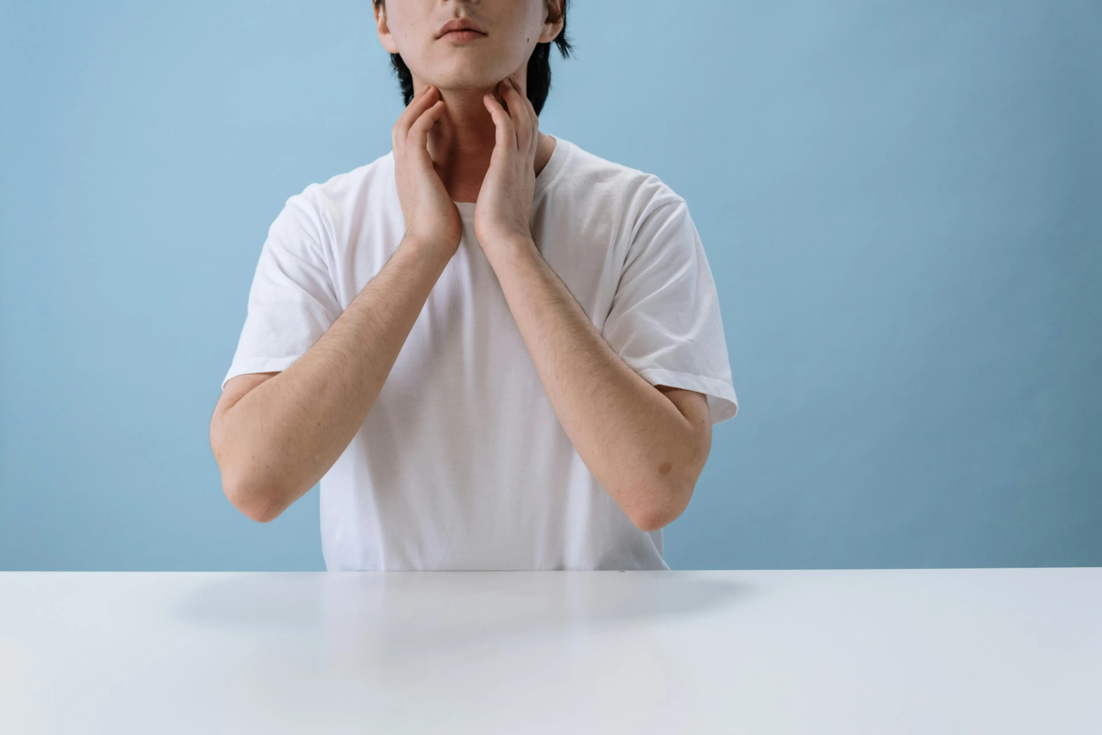 Person in a white shirt touching their throat, illustrating the human body quiz on the structure preventing food entering the windpipe.