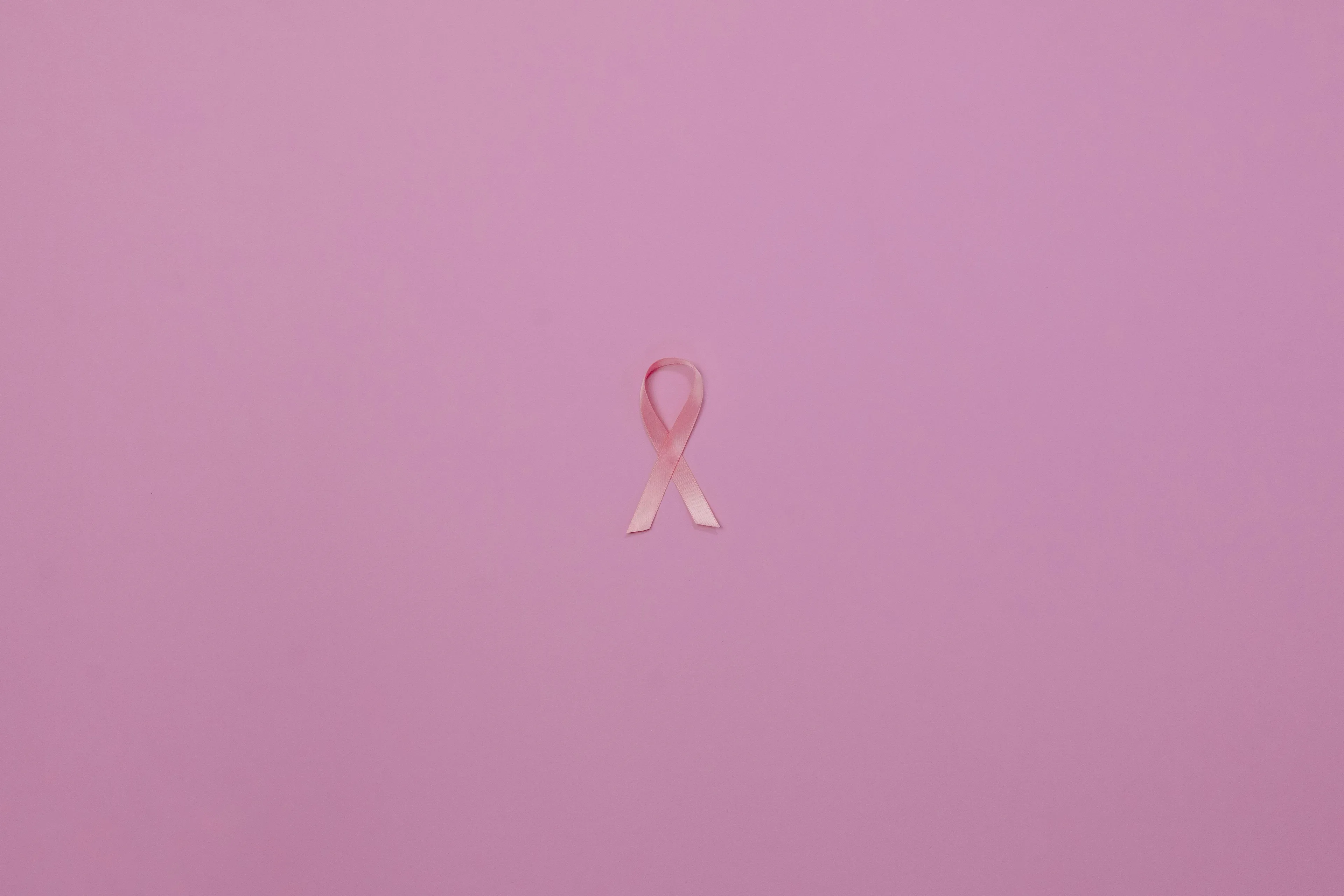 Pink breast cancer awareness ribbon on a simple pink background representing early detection in high school biology.