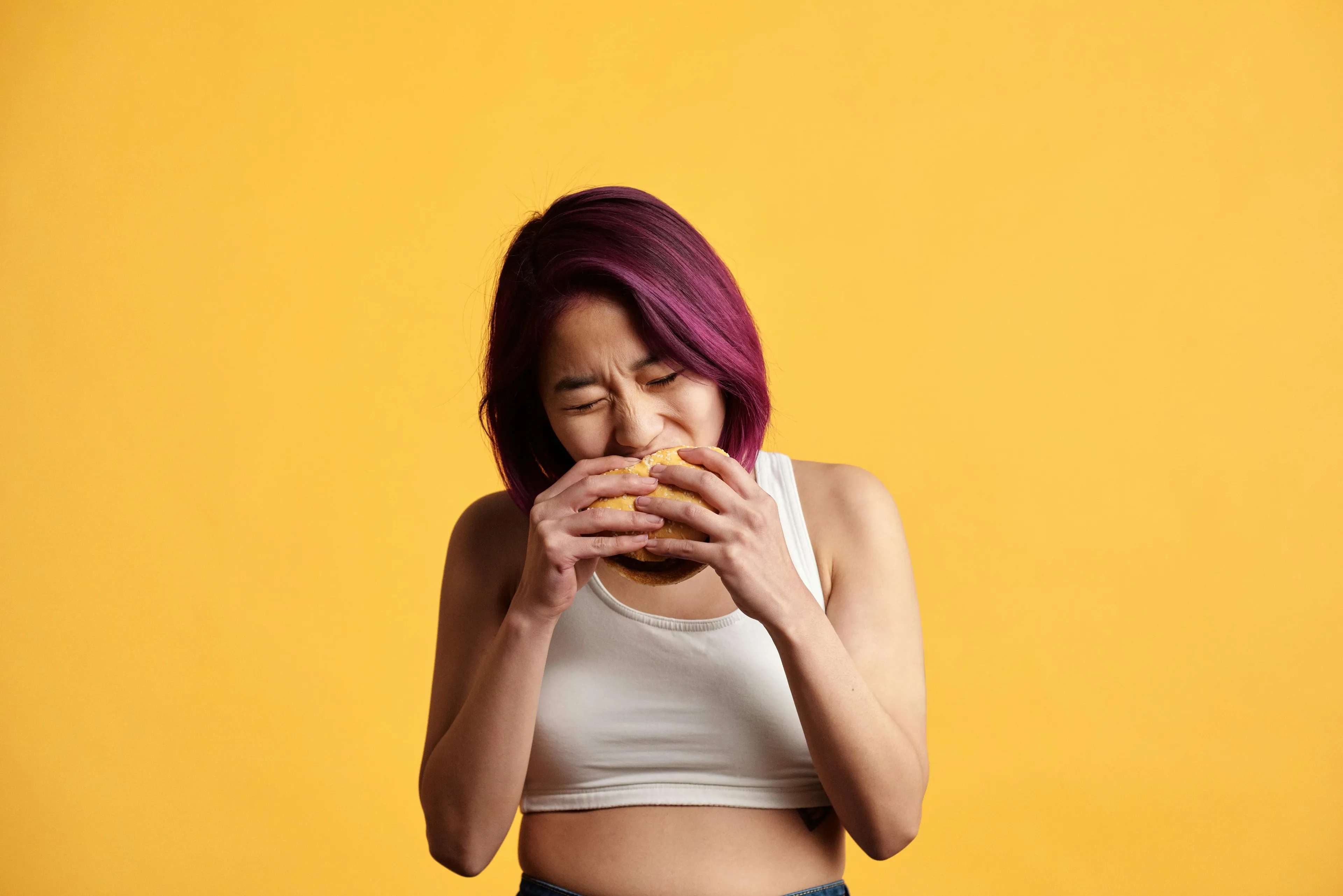 Young woman biting into a burger, representing the human body quiz concept on the center of appetite in biology.