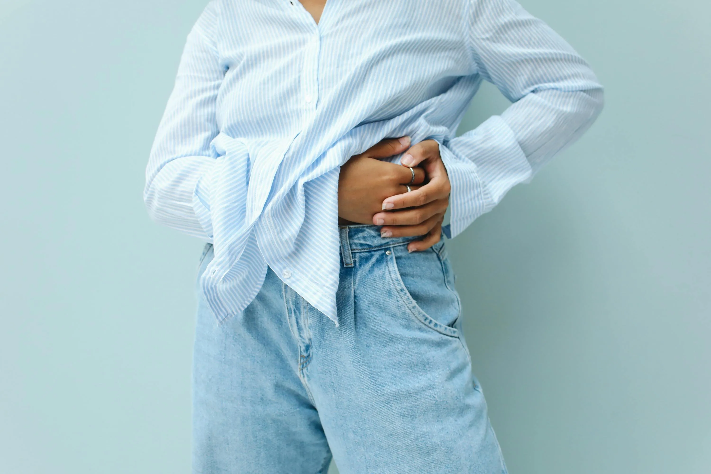 Person in a striped shirt and jeans holding their abdomen, illustrating human body digestion in high school biology quiz.
