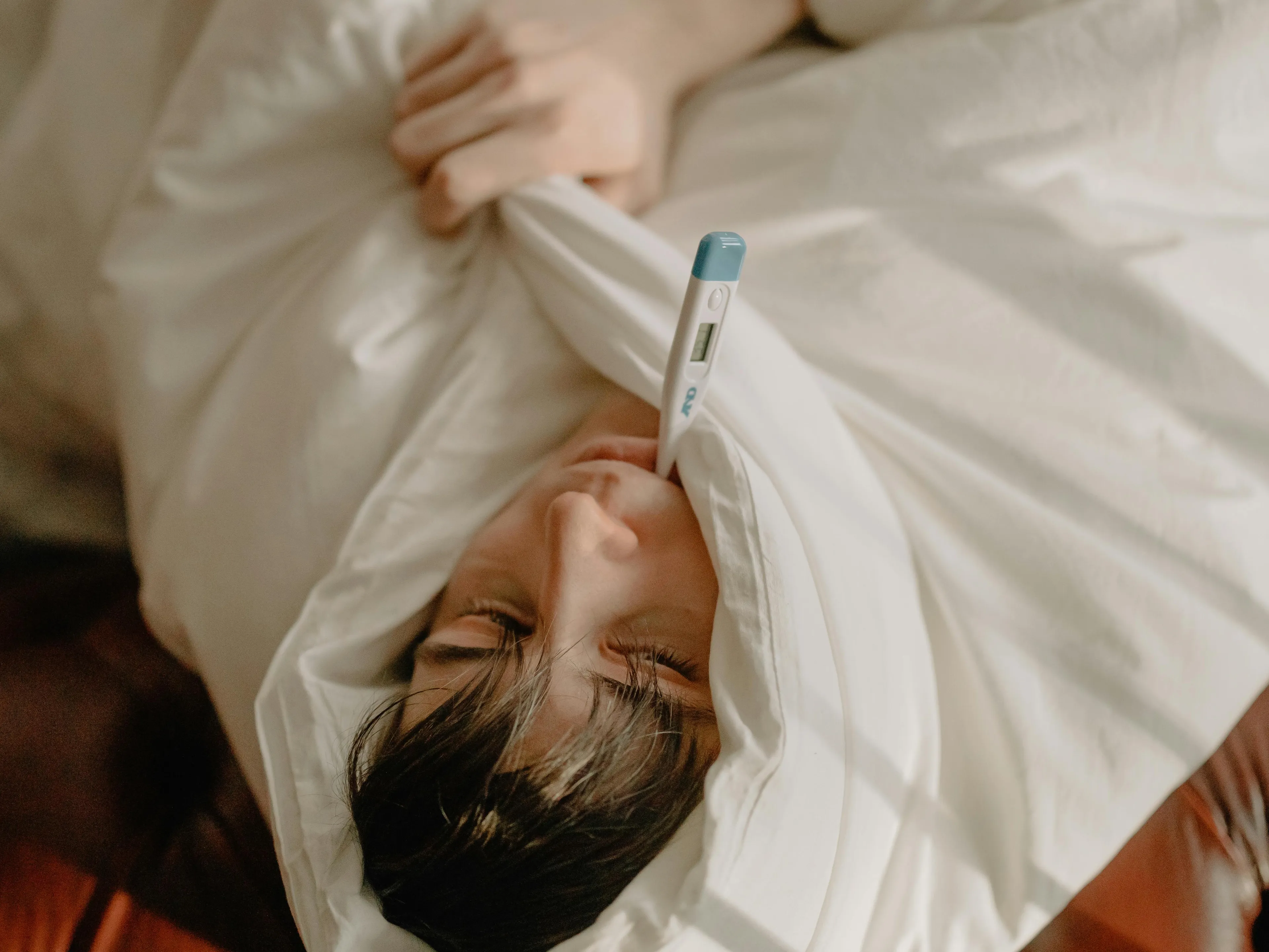 Teen wrapped in blanket with a thermometer on forehead, illustrating the human body quiz about fever symptoms and causes.