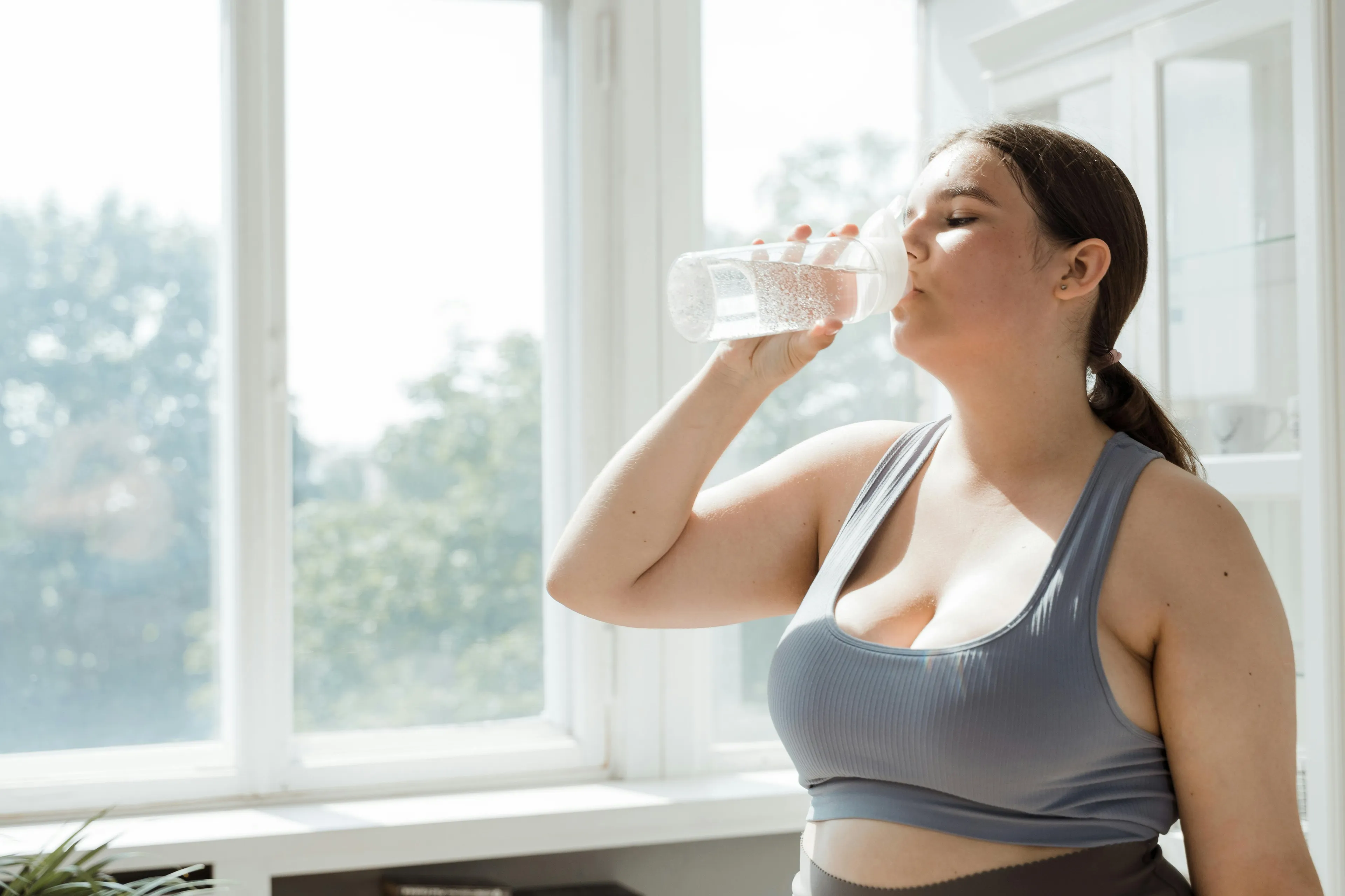 Young woman drinking water in bright room illustrating hormone responsible for maintaining water balance in the body.