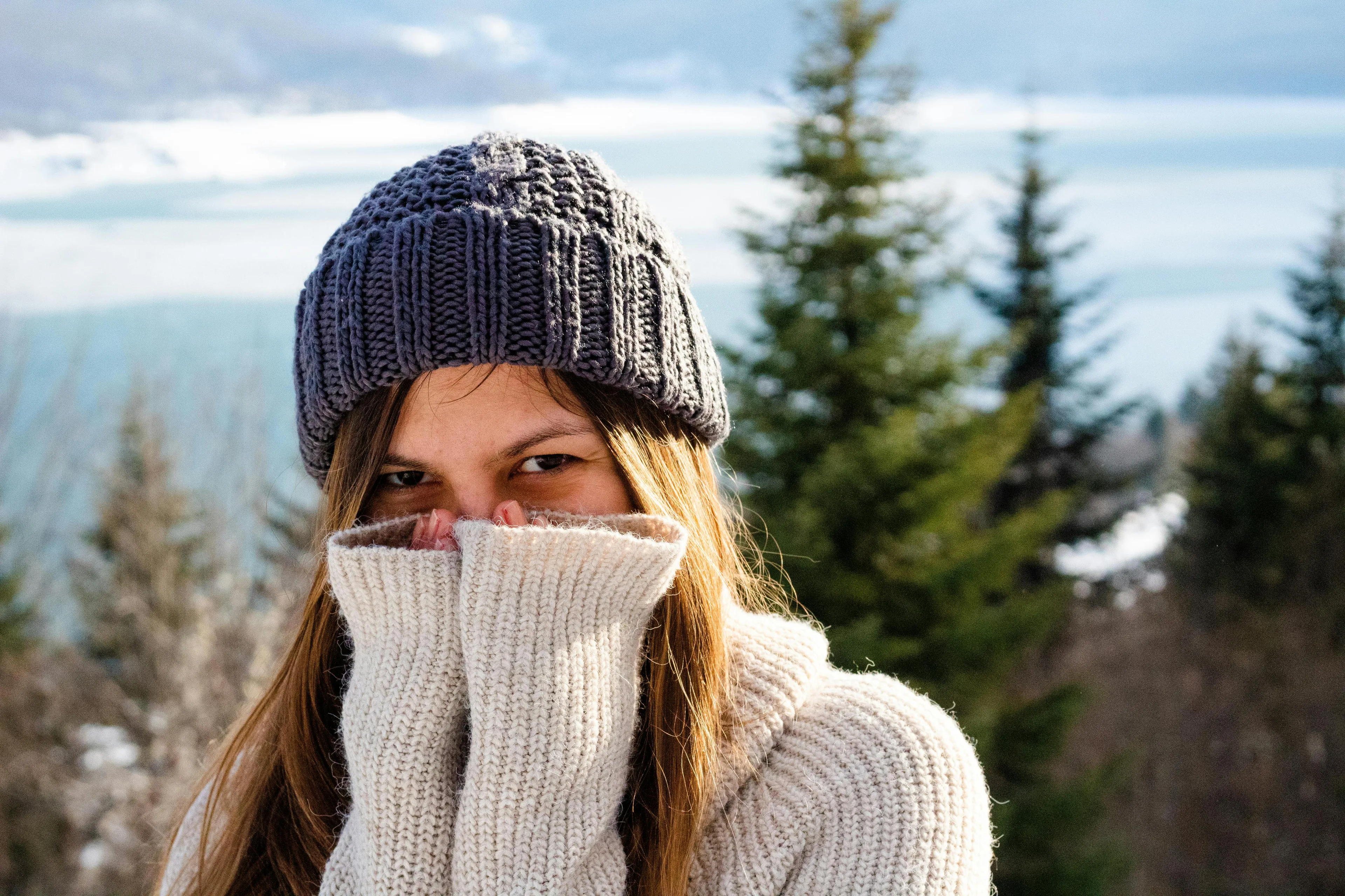 Young woman shivering in cold weather wearing a knit hat and sweater, illustrating the human body response to cold.
