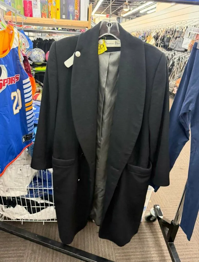 A black Christian Dior coat, a high-fashion thrift store jackpot find, hanging in a retail setting.