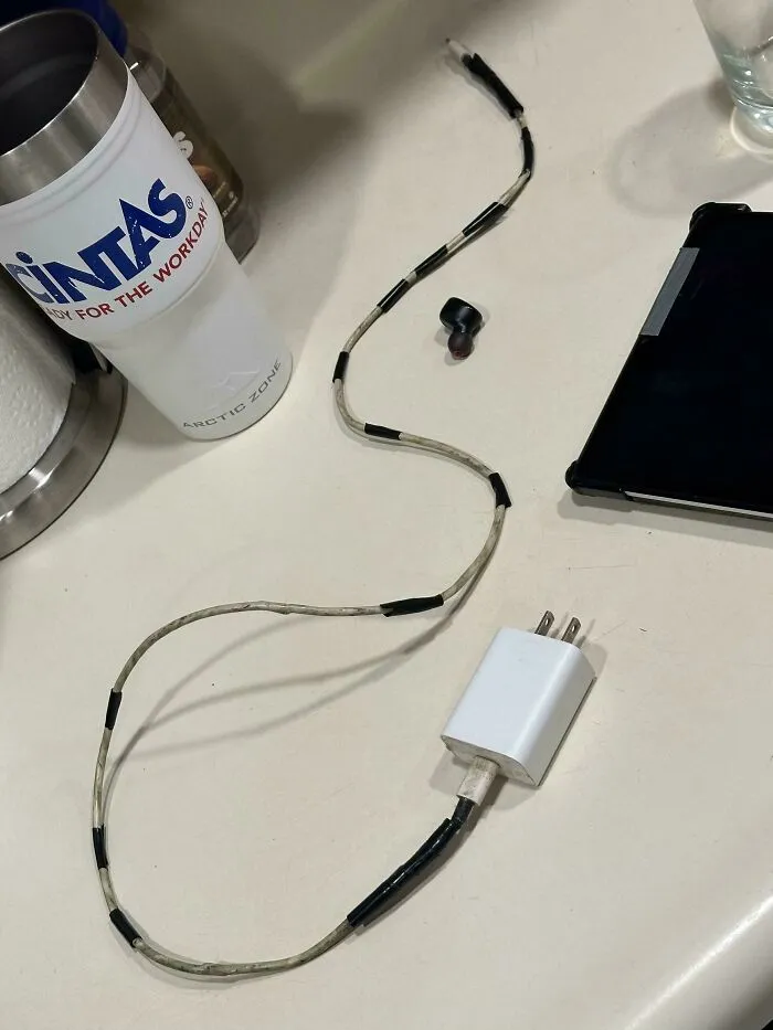 A makeshift phone charger and a GINTAS cup on a table, illustrating the reality of consumerism and price differences.
