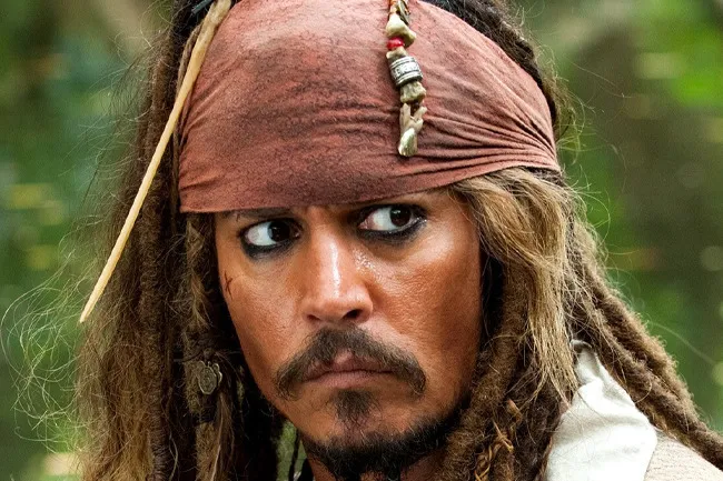 Close-up of Captain Jack Sparrow, looking intently, with his signature dreadlocks, brown bandana, and smudged eyeliner.