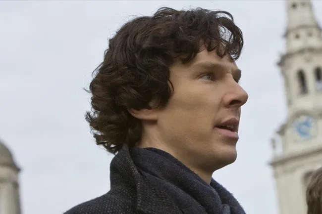 Benedict Cumberbatch as Sherlock Holmes, looking intently with a subtle blue scarf and dark coat, blurred city background.