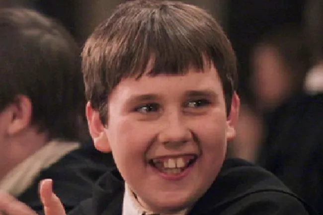 A young Neville Longbottom with short brown hair, a wide gap-toothed smile, and wearing dark robes.