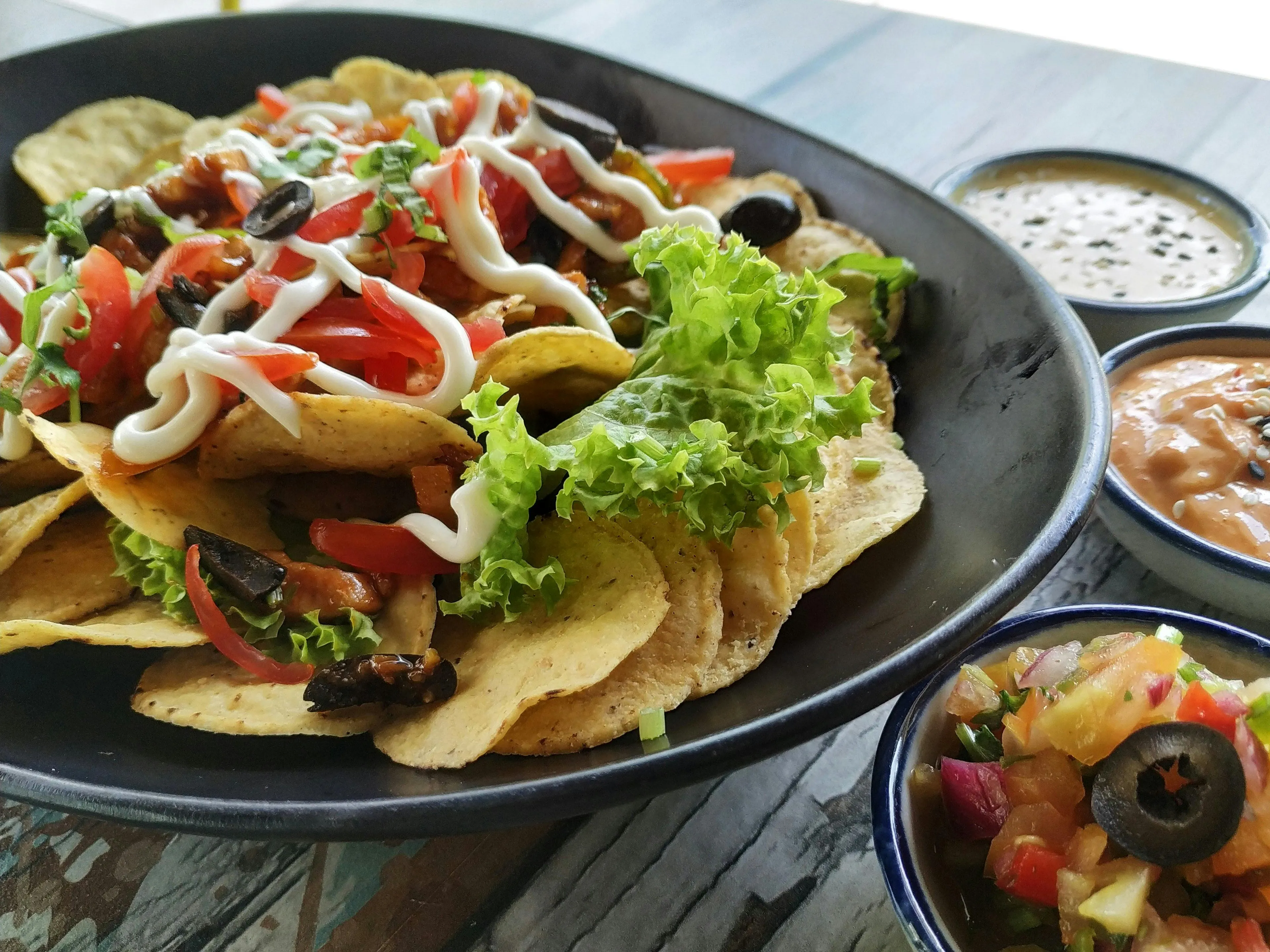 Delicious nachos topped with fresh tomatoes, olives, lettuce, and creamy sauce, served with three dipping bowls. Comfort food when the day goes south.
