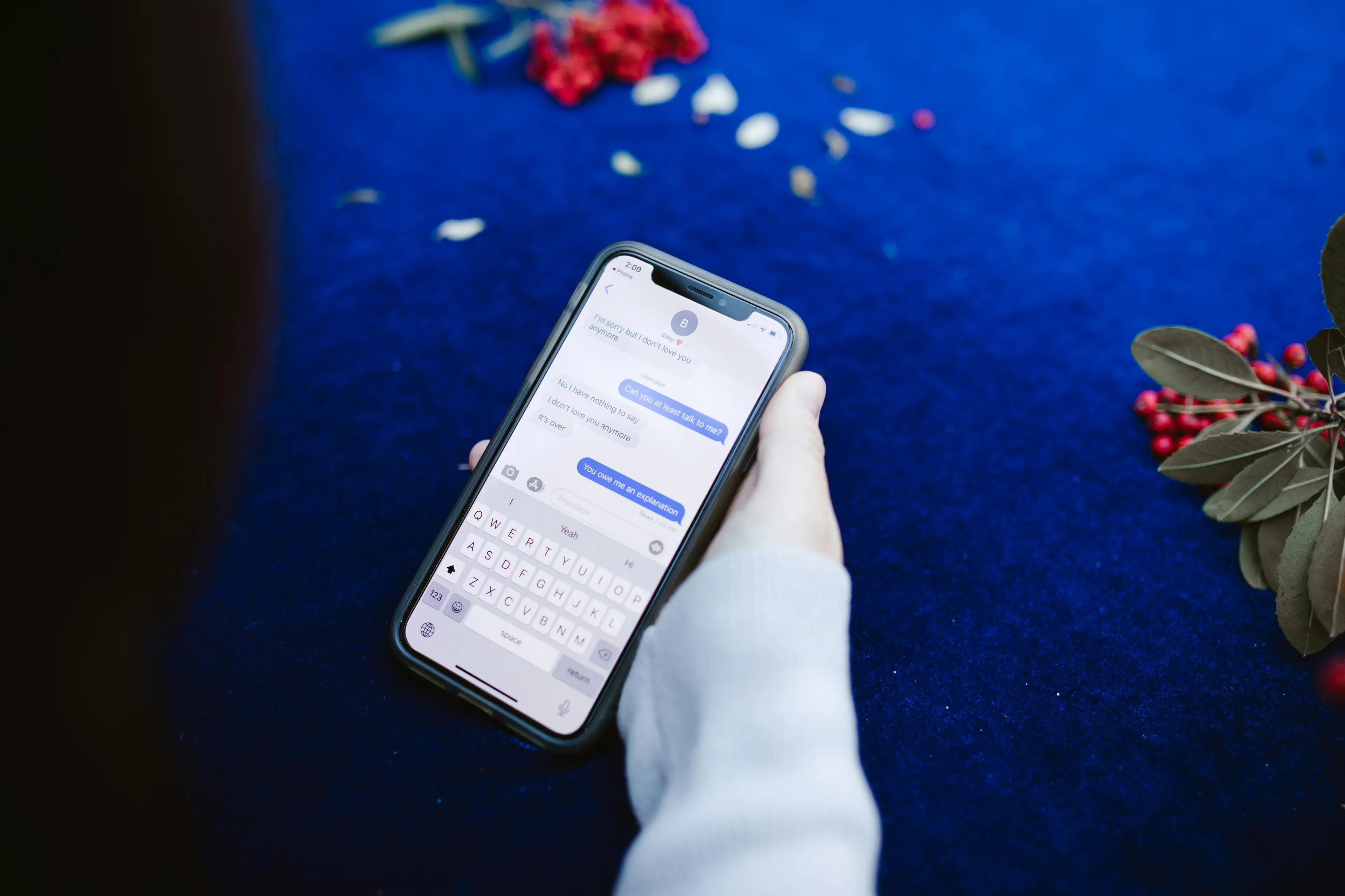 A person holding a phone, texting on a blue surface with red berries. Great for a rainy-day activity to catch up on unread messages.