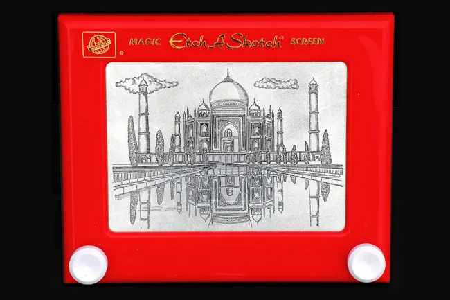 A red Etch A Sketch toy with a detailed drawing of the Taj Mahal and its reflection, showcasing nostalgic fun.