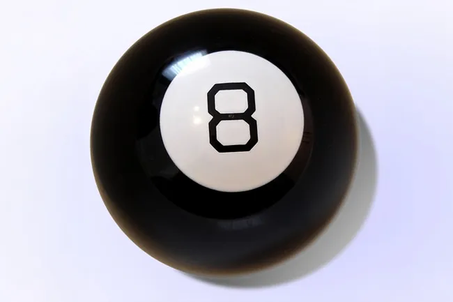 A close-up shot of a classic black Magic 8 Ball, featuring the white circle with the number 8 on a light background. Nostalgic toy.