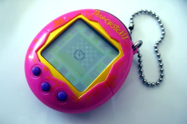 A pink Tamagotchi, a nostalgic toy, with yellow trim, purple buttons, and a small digital pet on the screen.