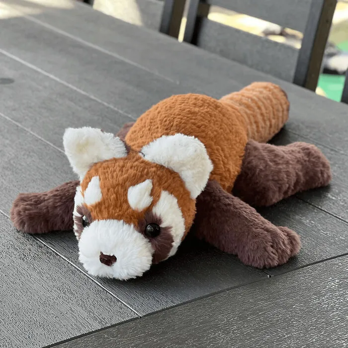 Crocheted red panda plush toy lying flat on a wooden table