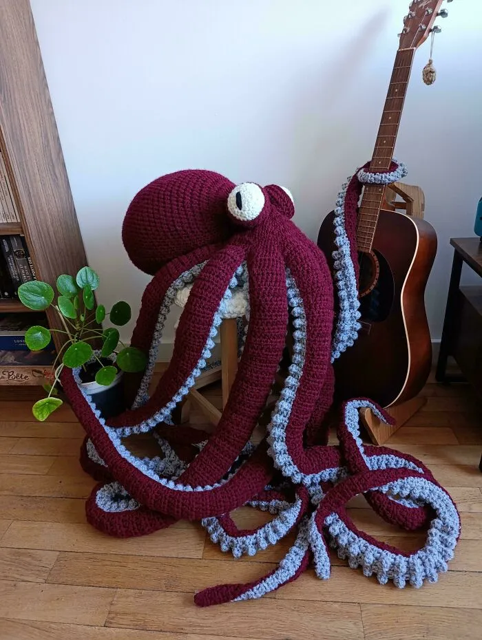 Large crocheted octopus plush with maroon and gray yarn next to an acoustic guitar