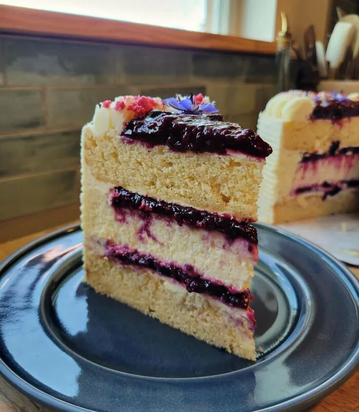 Slice of vanilla cake with berry filling and frosting on a plate