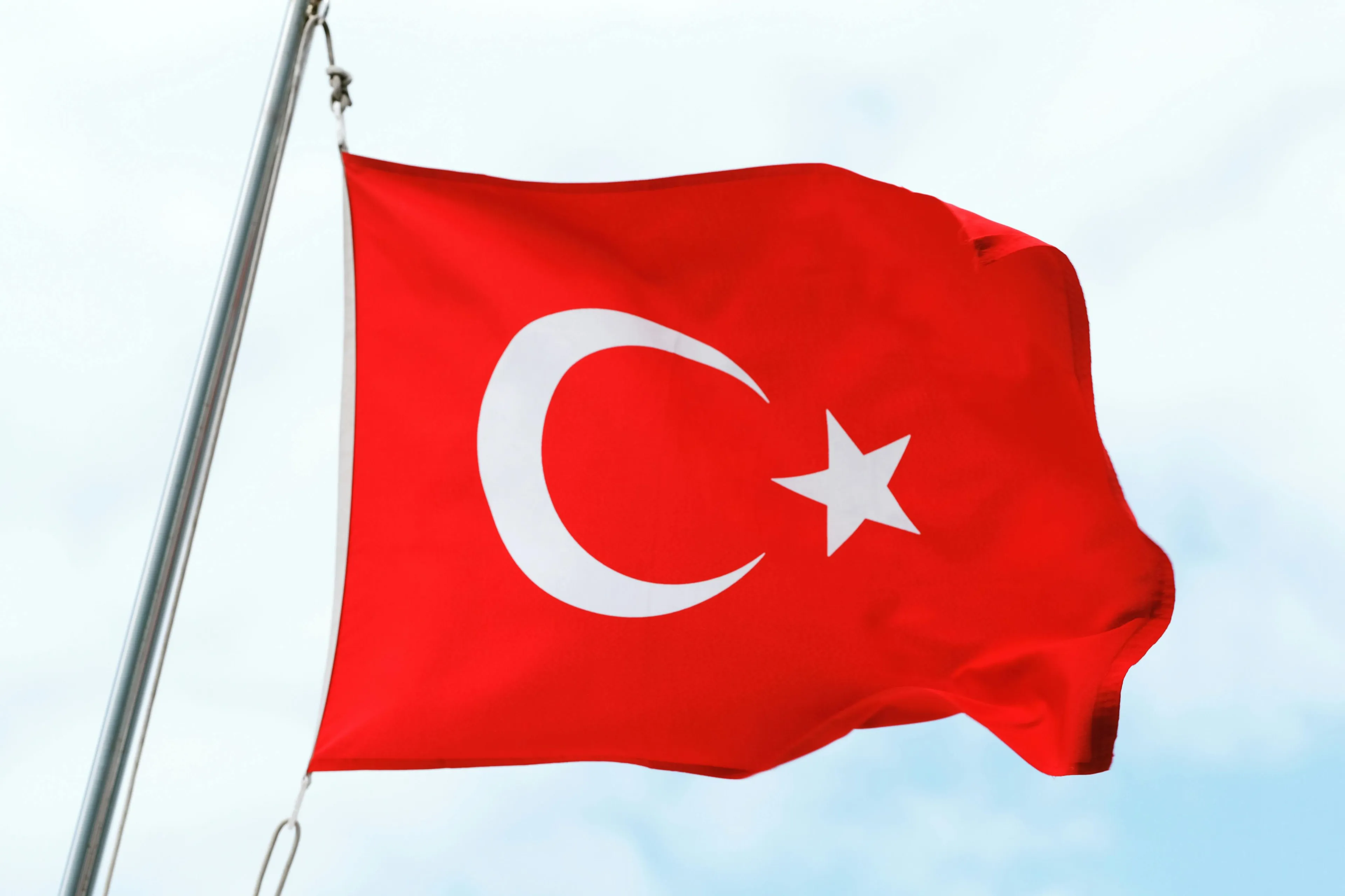 The red flag of Turkey, with its white crescent and star, waving against a light blue sky. Trivia Night question.