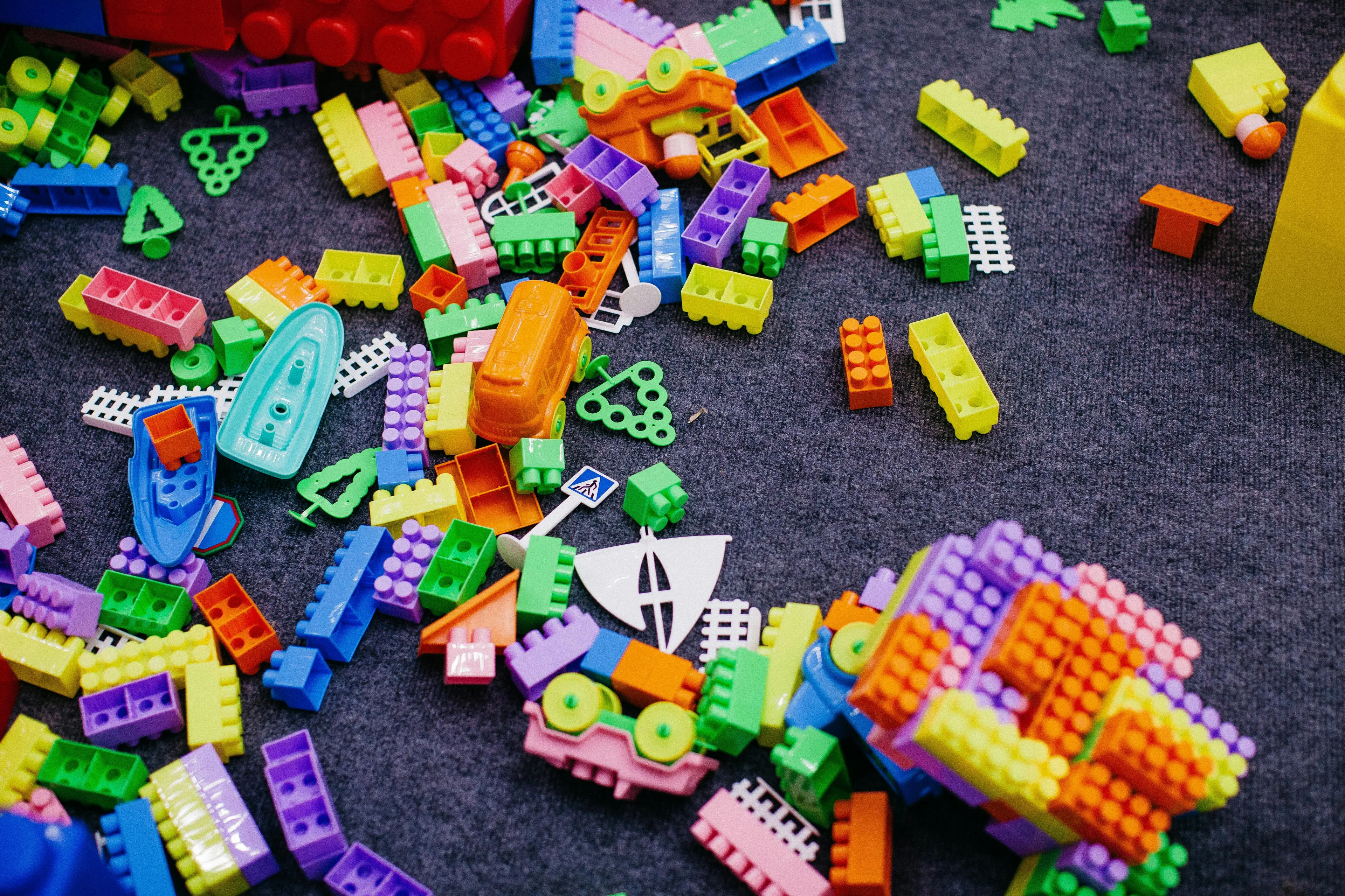 Colorful LEGO-like building blocks scattered on a gray carpet, including boats and vehicle parts, sparking trivia night fun.