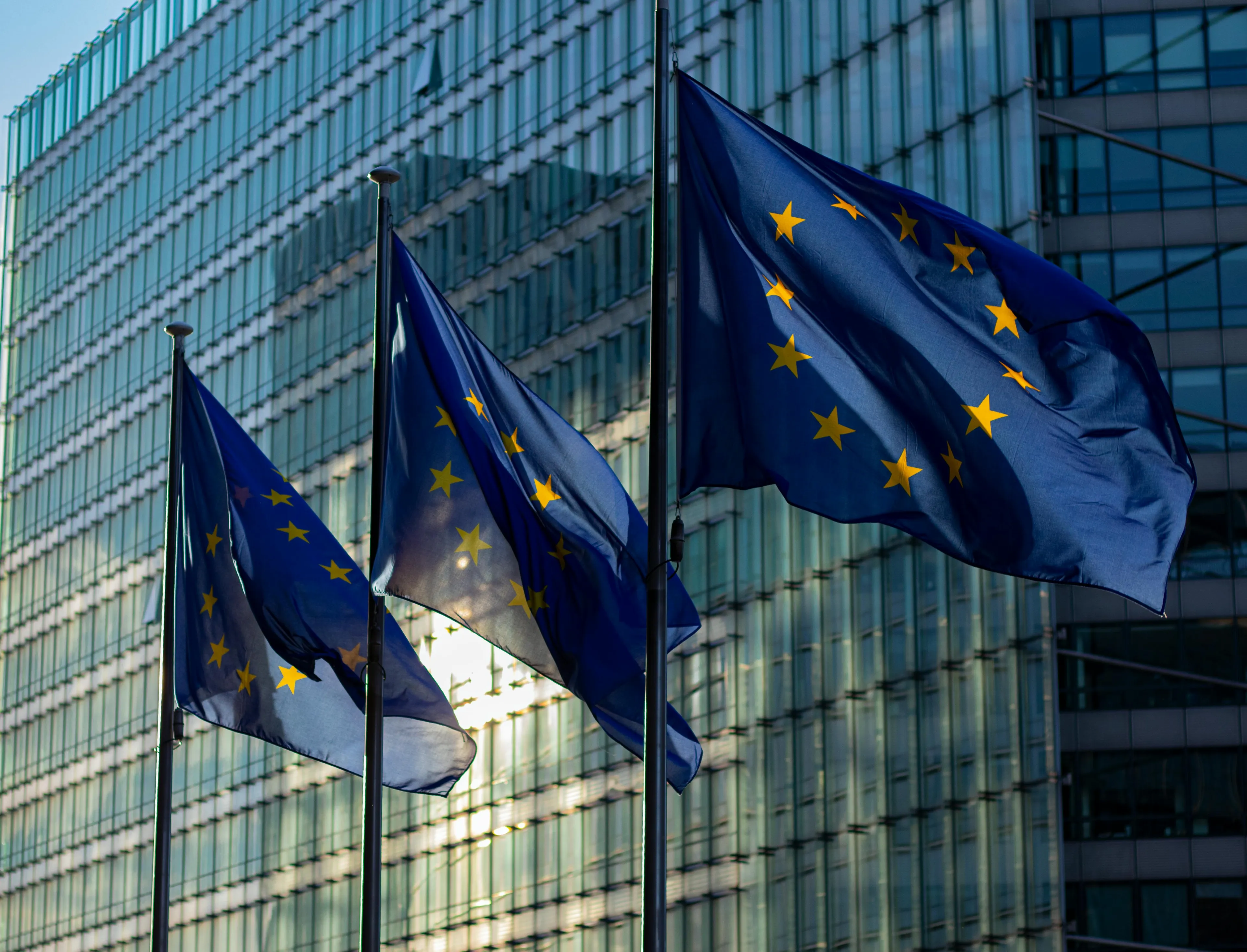 Three European Union flags fly in front of a modern glass building. Can you win trivia night?