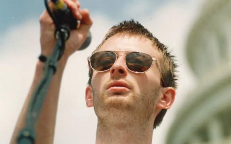 Thom Yorke, lead singer, wearing sunglasses and holding a microphone, performing outdoors. Test your Trivia Night knowledge!