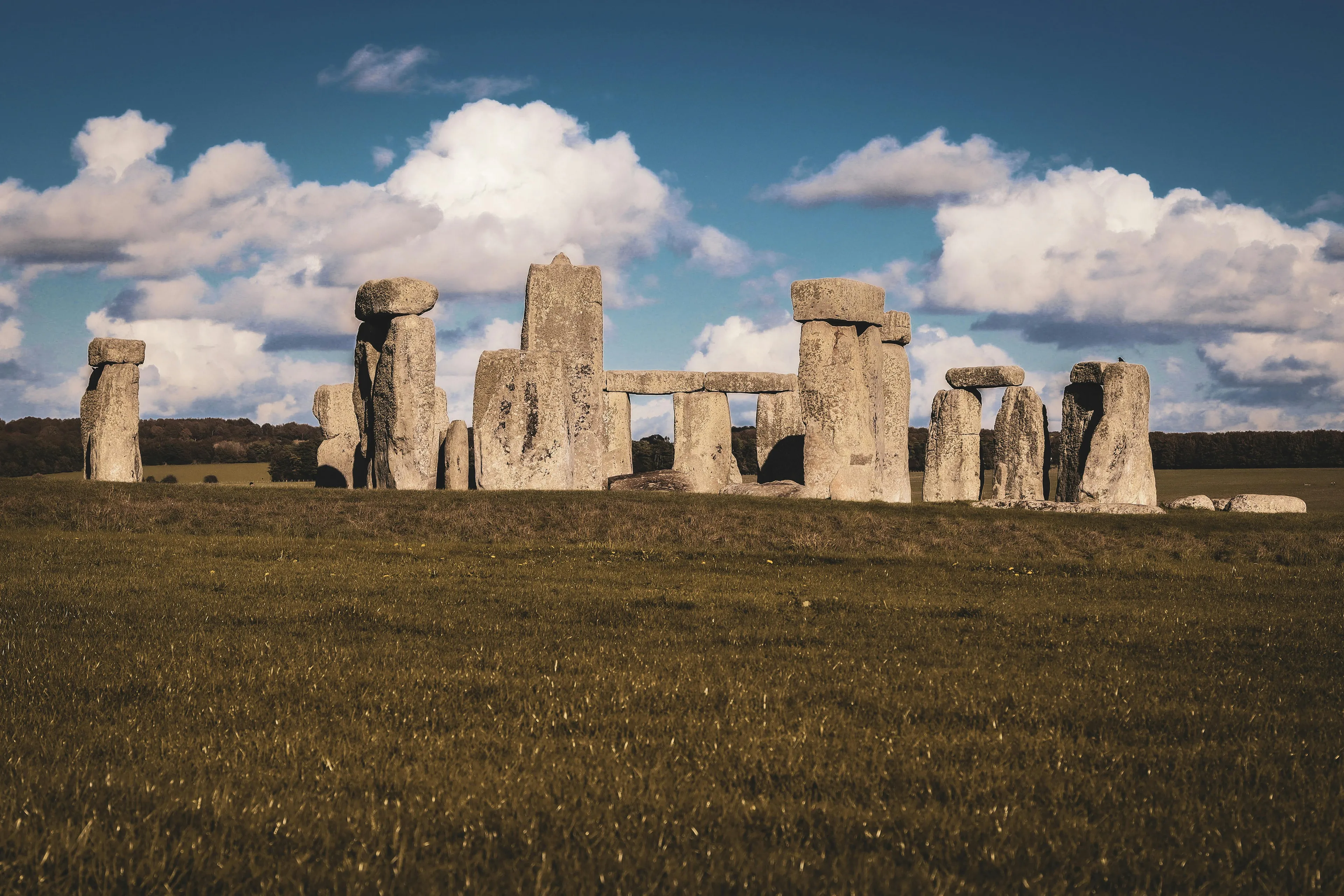 Ancient Stonehenge structure in a grassy field under a cloudy blue sky. Can you name this structure? Win Trivia Night.