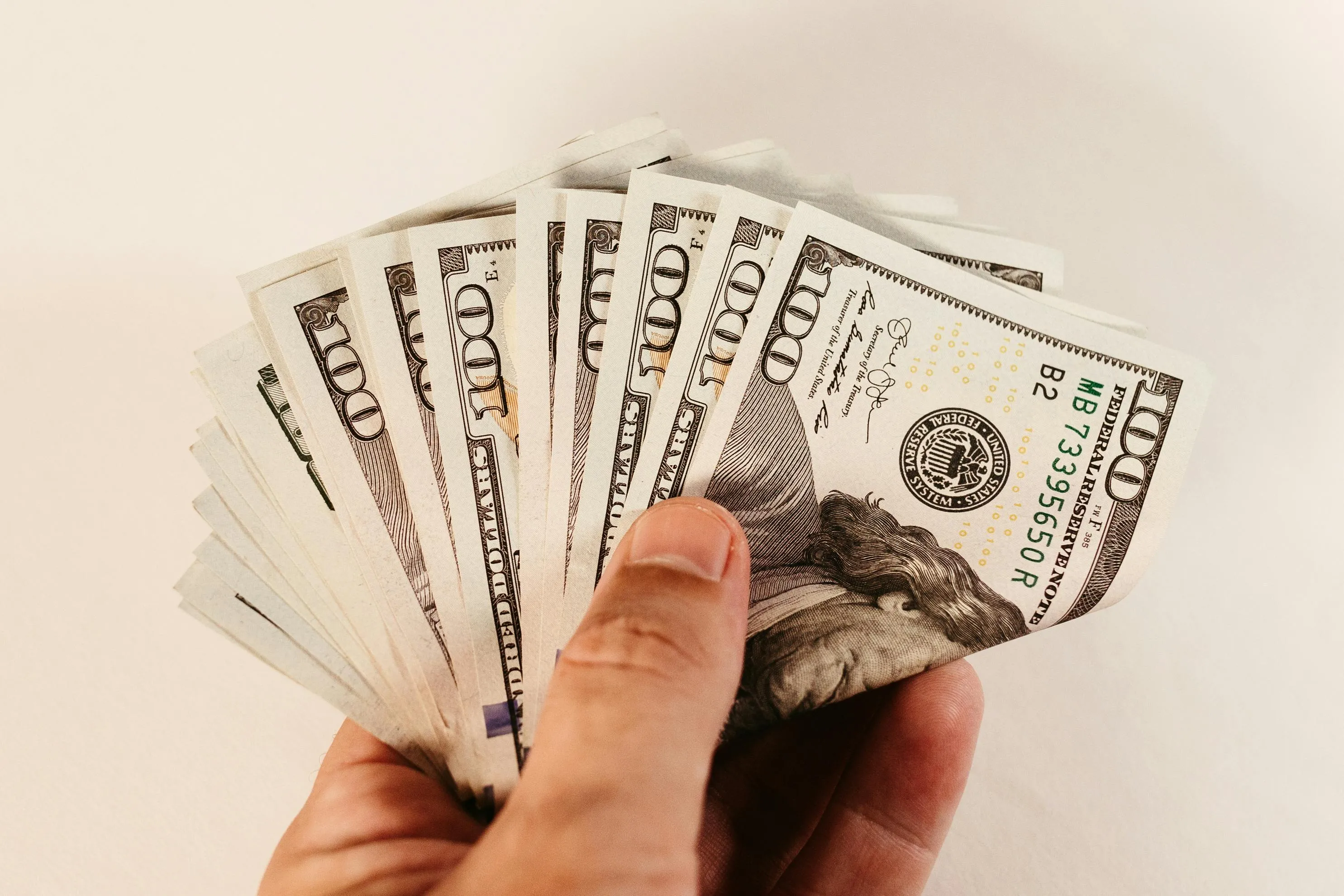 A hand holding a fanned stack of US hundred dollar bills. A great housewarming gift idea for those who prefer cash.