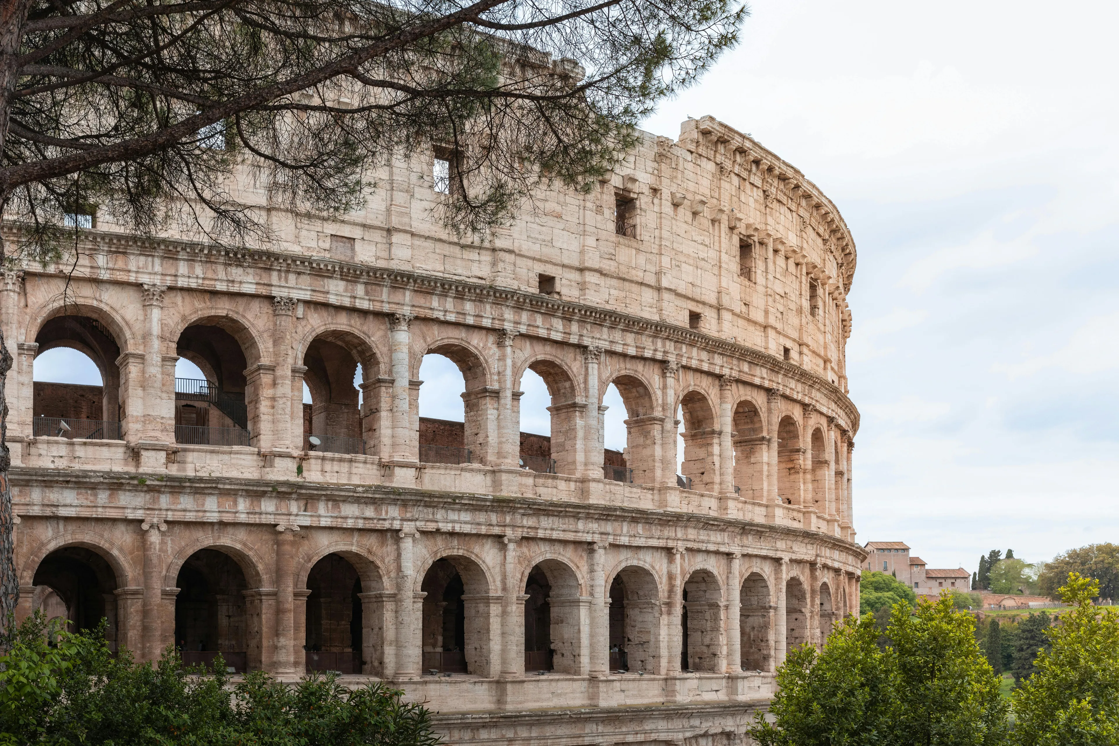 The Colosseum in Rome, a multi-story stone amphitheater, features a facade of arches and columns under a cloudy sky.