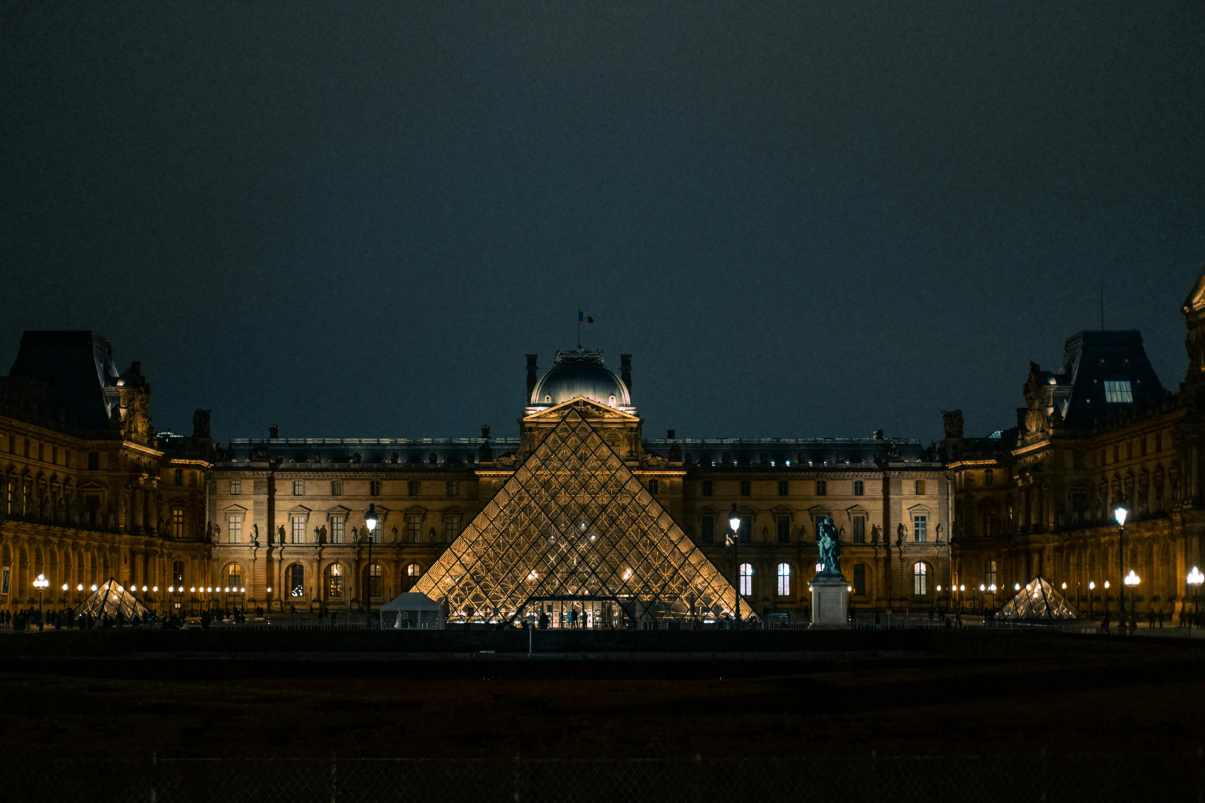 The Louvre pyramid and museum illuminated at night, showcasing the iconic landmark's grandeur against a dark sky.