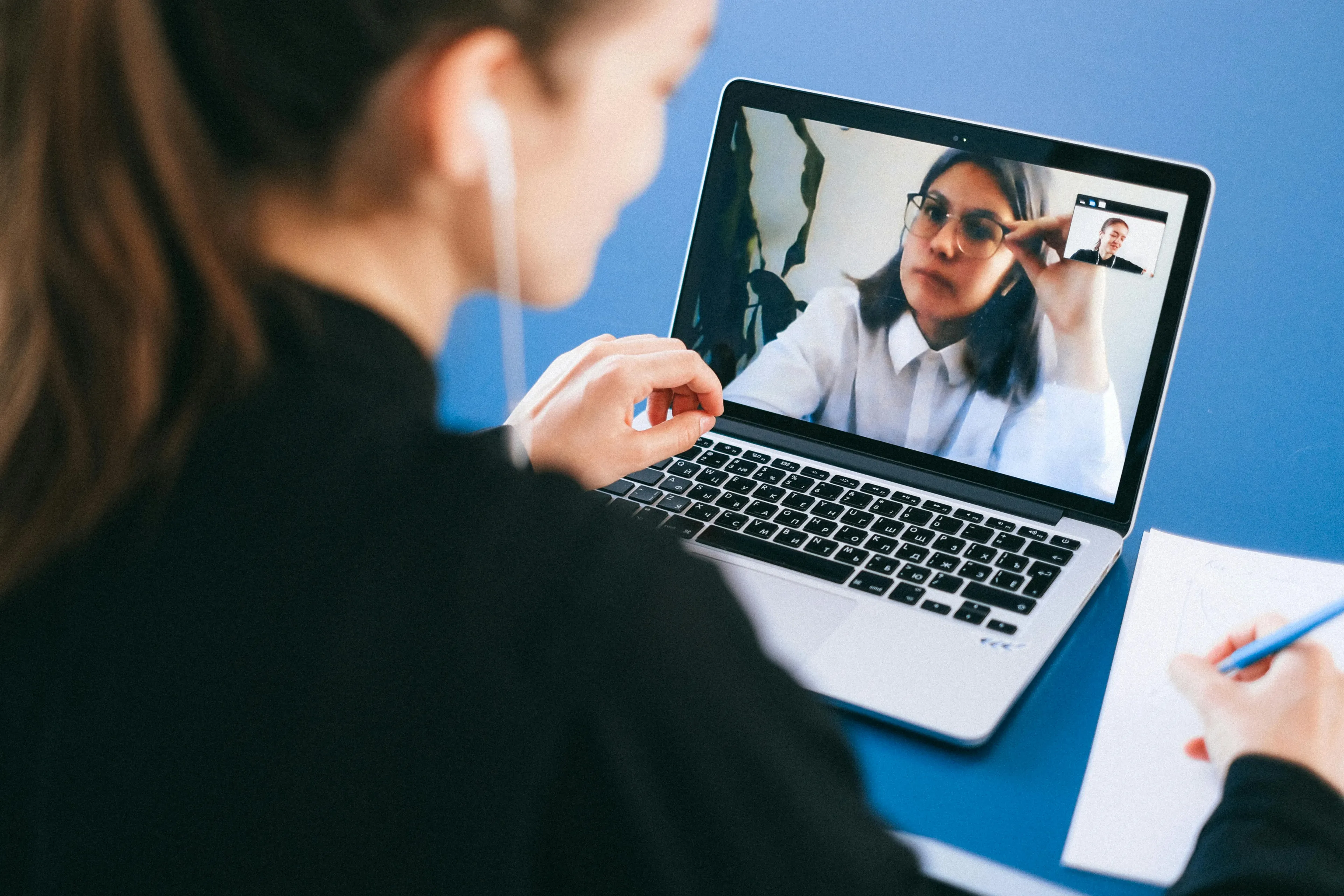 Person on laptop in a Zoom meeting, with visible earbuds, writing notes. Quiz your reaction to rejection.