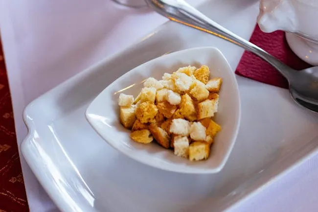 A small white dish filled with golden-brown croutons, ready to pick a soup topping or add extra crackers.