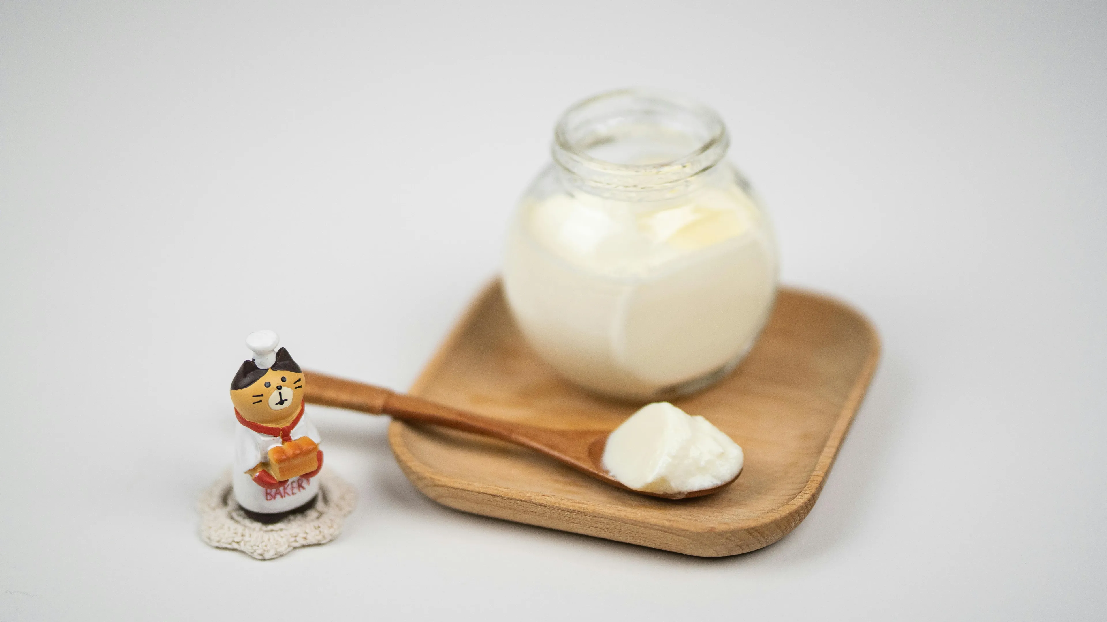 A jar of sour cream and a spoonful of it on a wooden tray, perfect as a soup topping. A chef cat figurine is nearby.