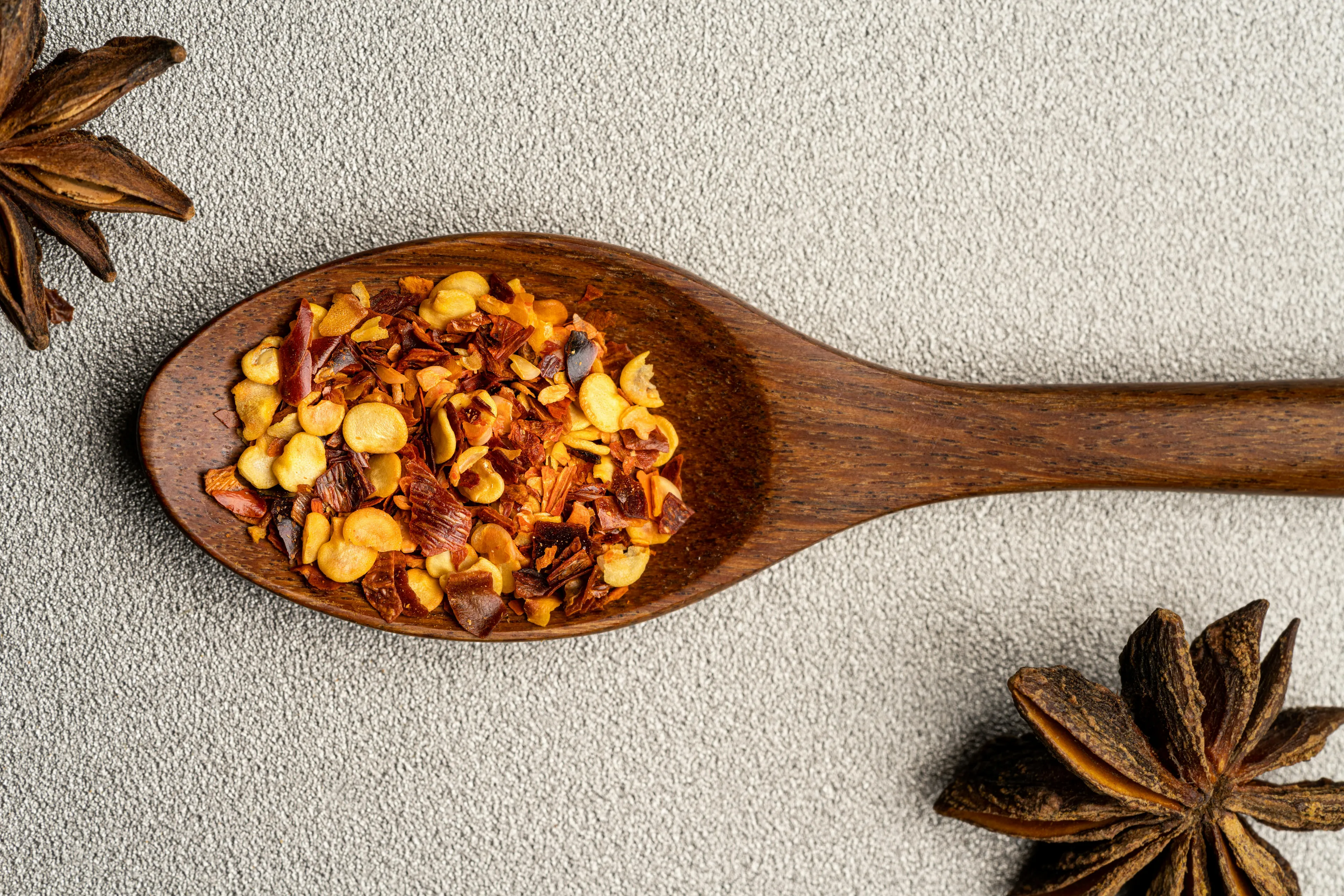 A wooden spoon holds chili flakes, an excellent soup topping, on a textured background with star anise.