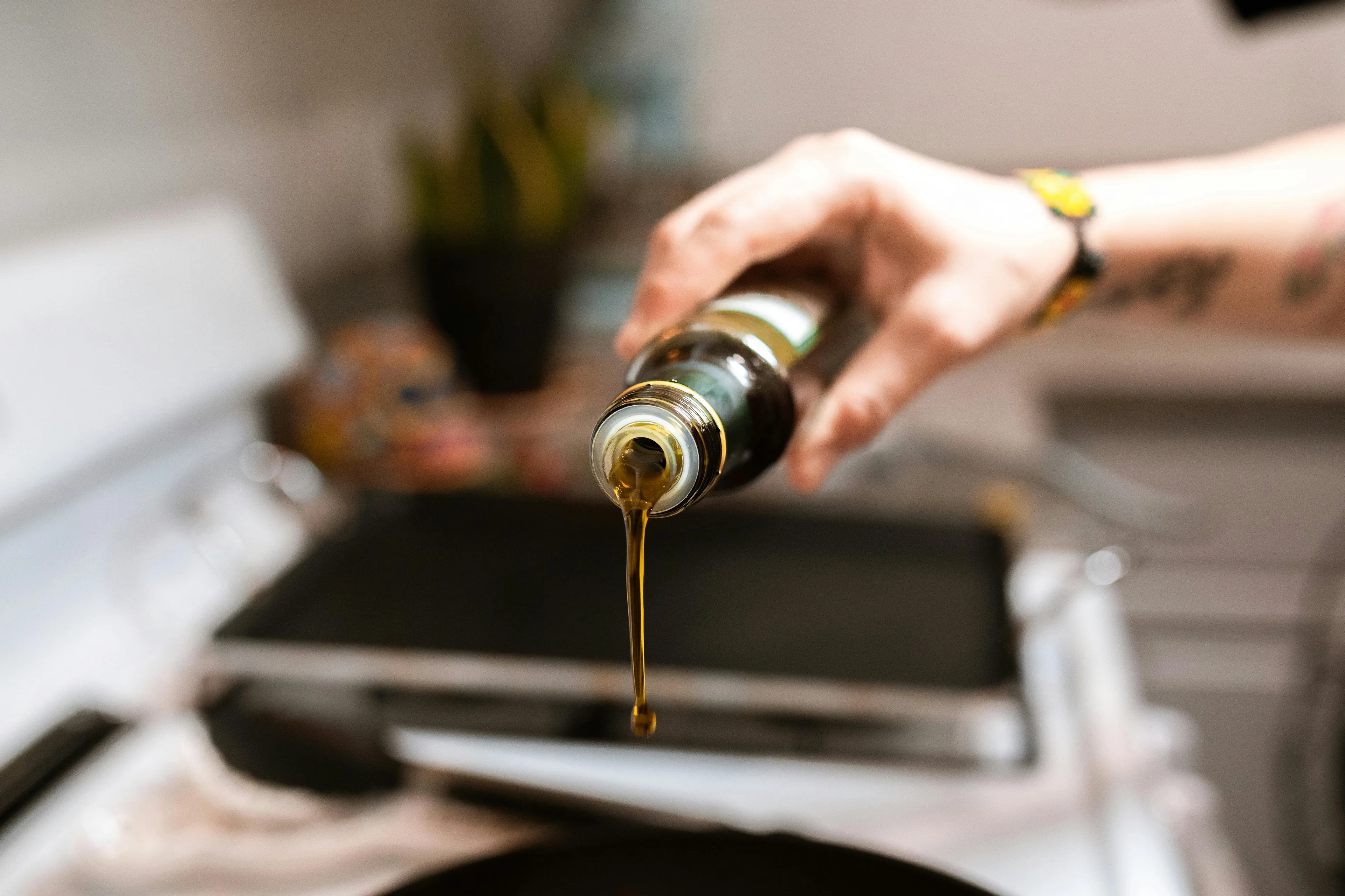 A hand drizzles olive oil from a dark bottle into a pan, a great soup topping idea.