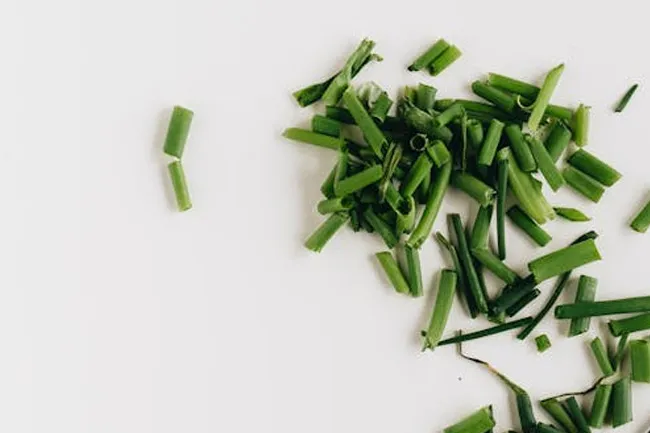 Freshly chopped chives scattered on a white surface, ideal for a soup topping.