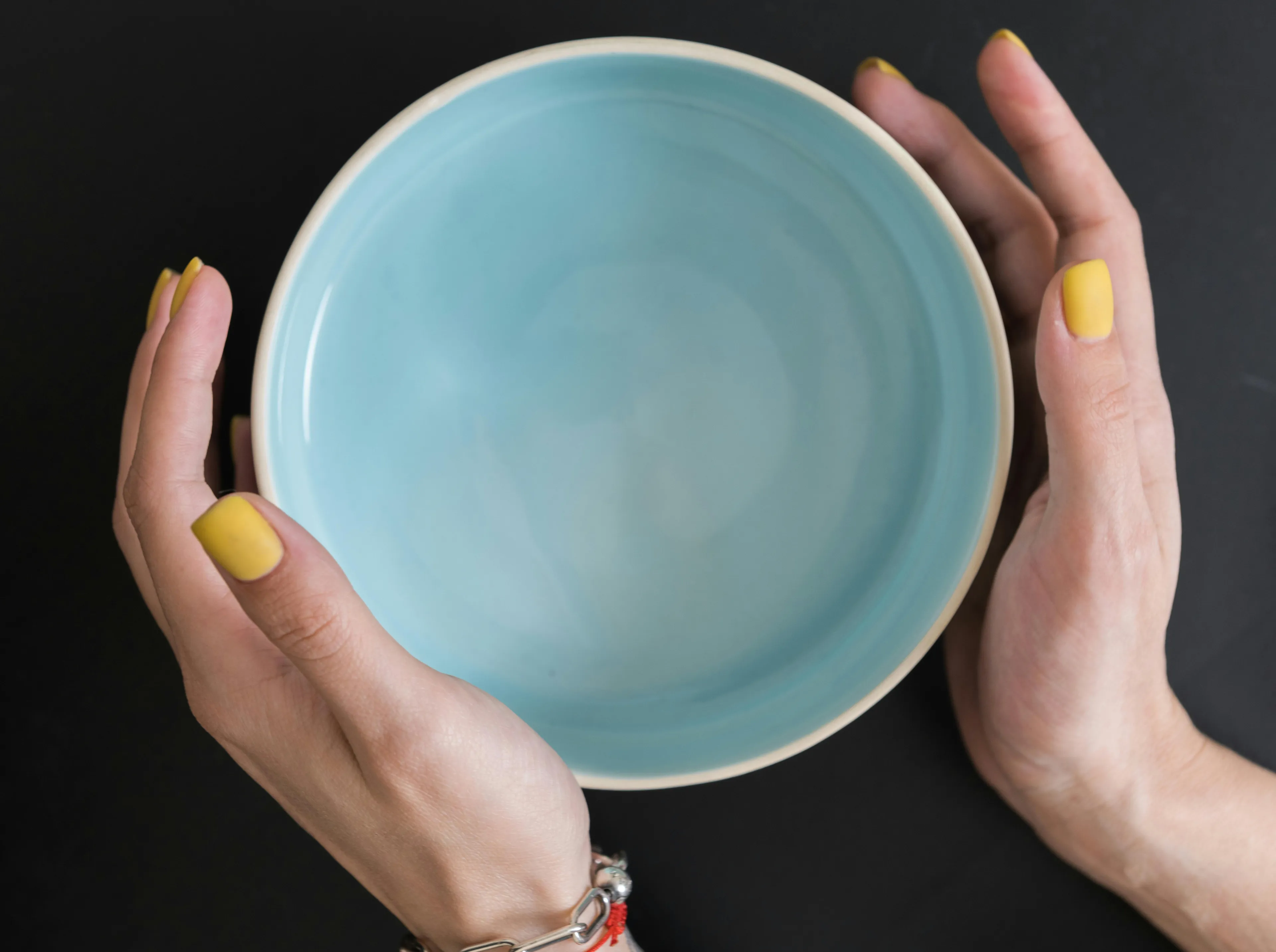 A woman's hands with yellow nail polish holding an empty blue bowl, ready for a soup topping.