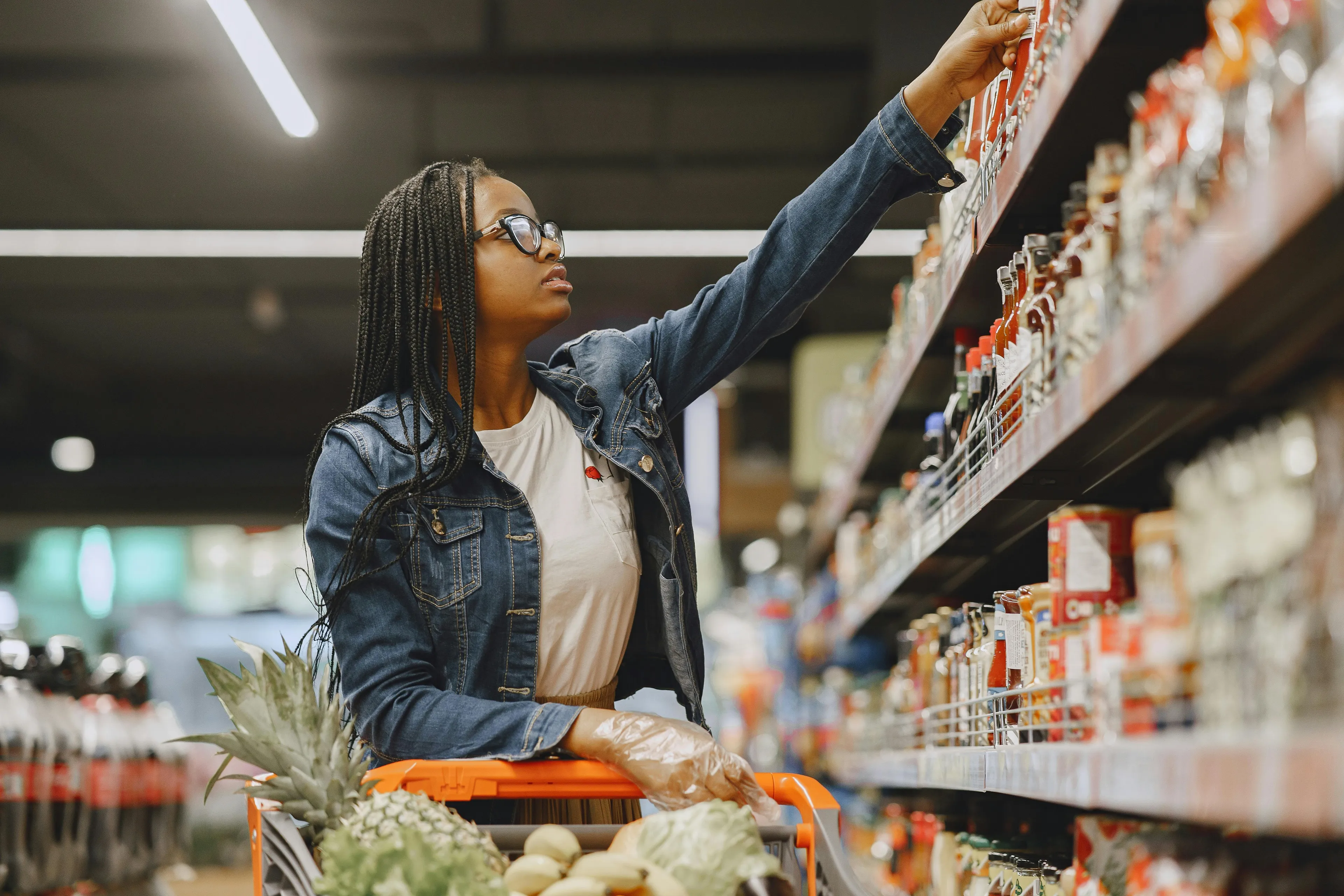 Woman in a denim jacket and glasses reaching for a product in a grocery store. Learning how to apologize.