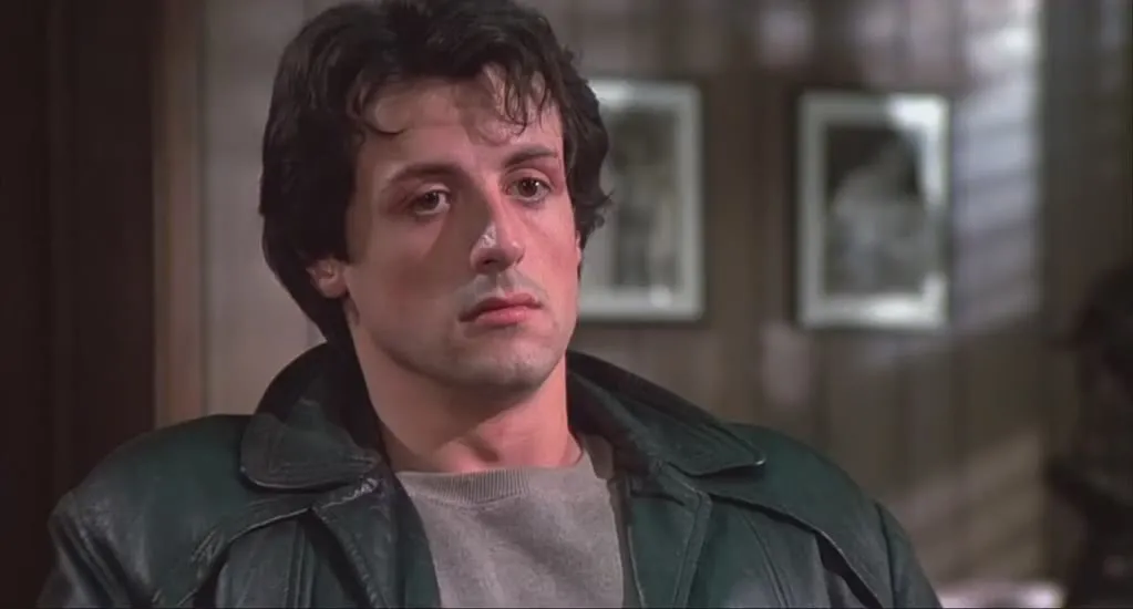 A young Rocky Balboa, looking contemplative, with slight bruising, wearing a dark green leather jacket. A comfort movie choice.