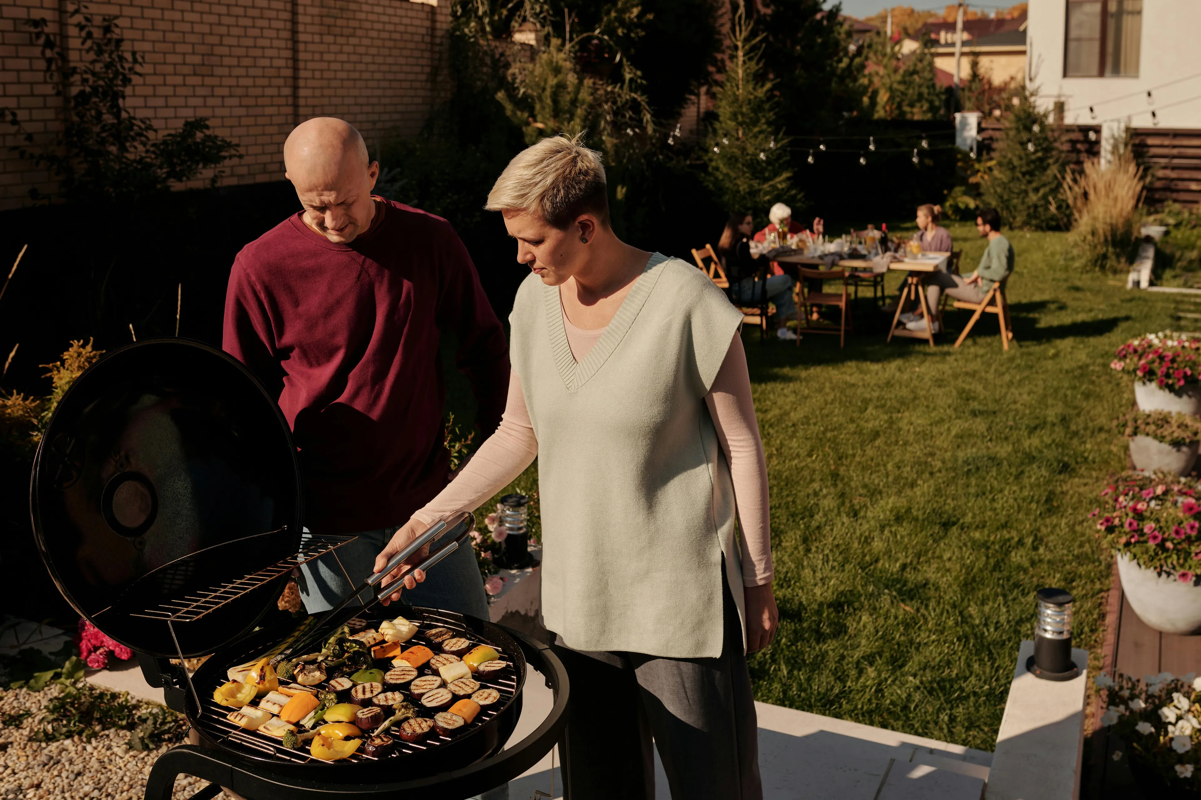 Man and woman grilling vegetables at a backyard BBQ, with blurred guests in the background. A reaction to rejection quiz scenario.