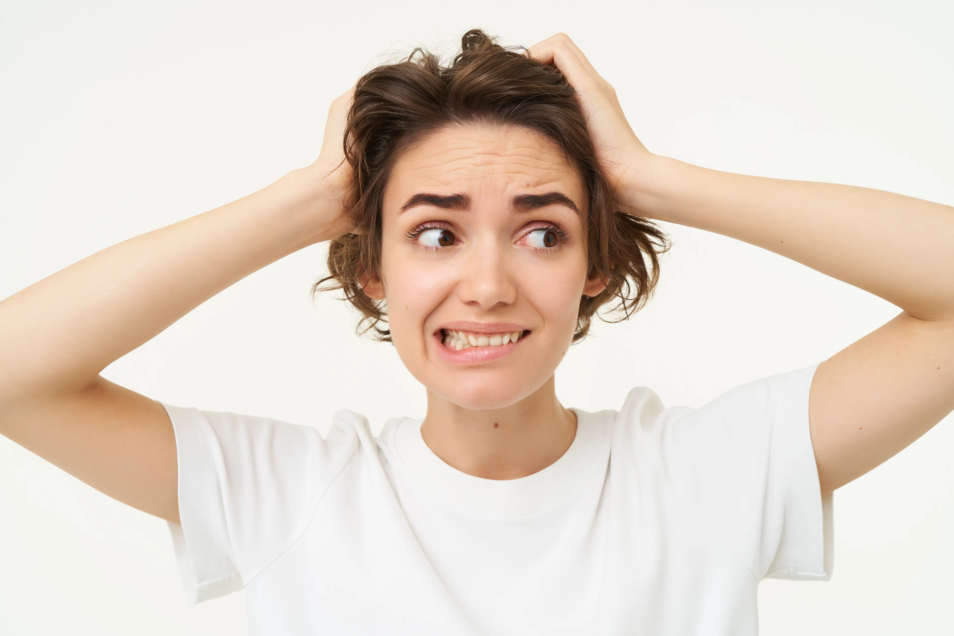 A worried woman with short brown hair clutches her head, biting her lip, demonstrating how to apologize.
